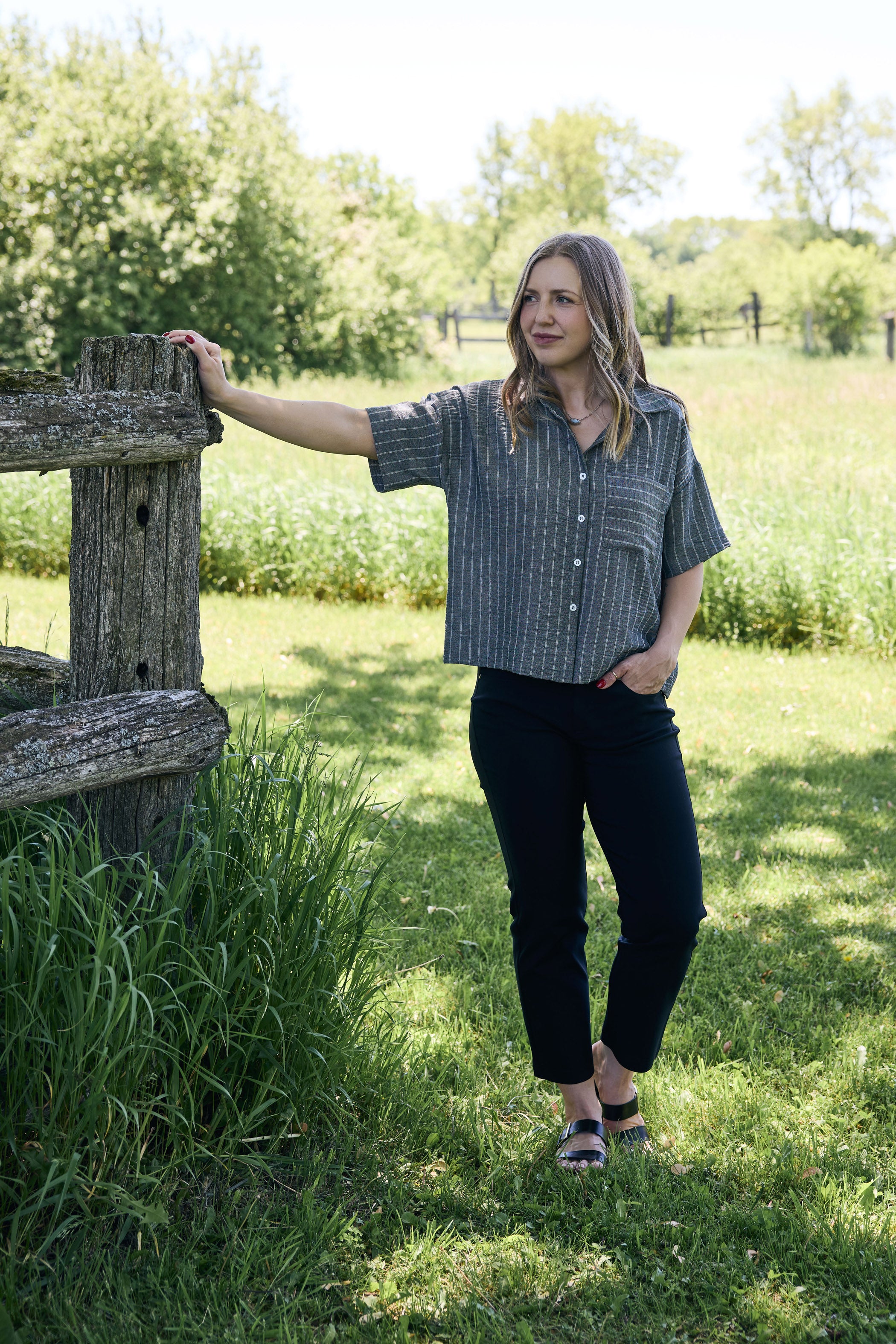 Woman standing outdoors in a grassy area with trees in the background