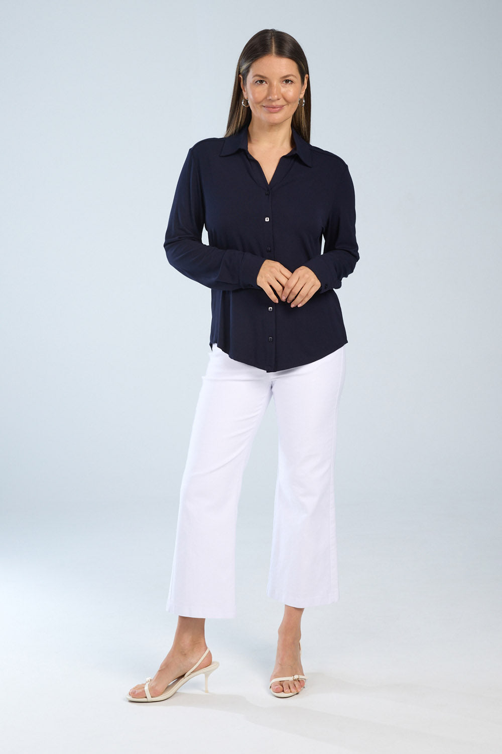 Woman wearing a navy shirt and white pants on a light gray background