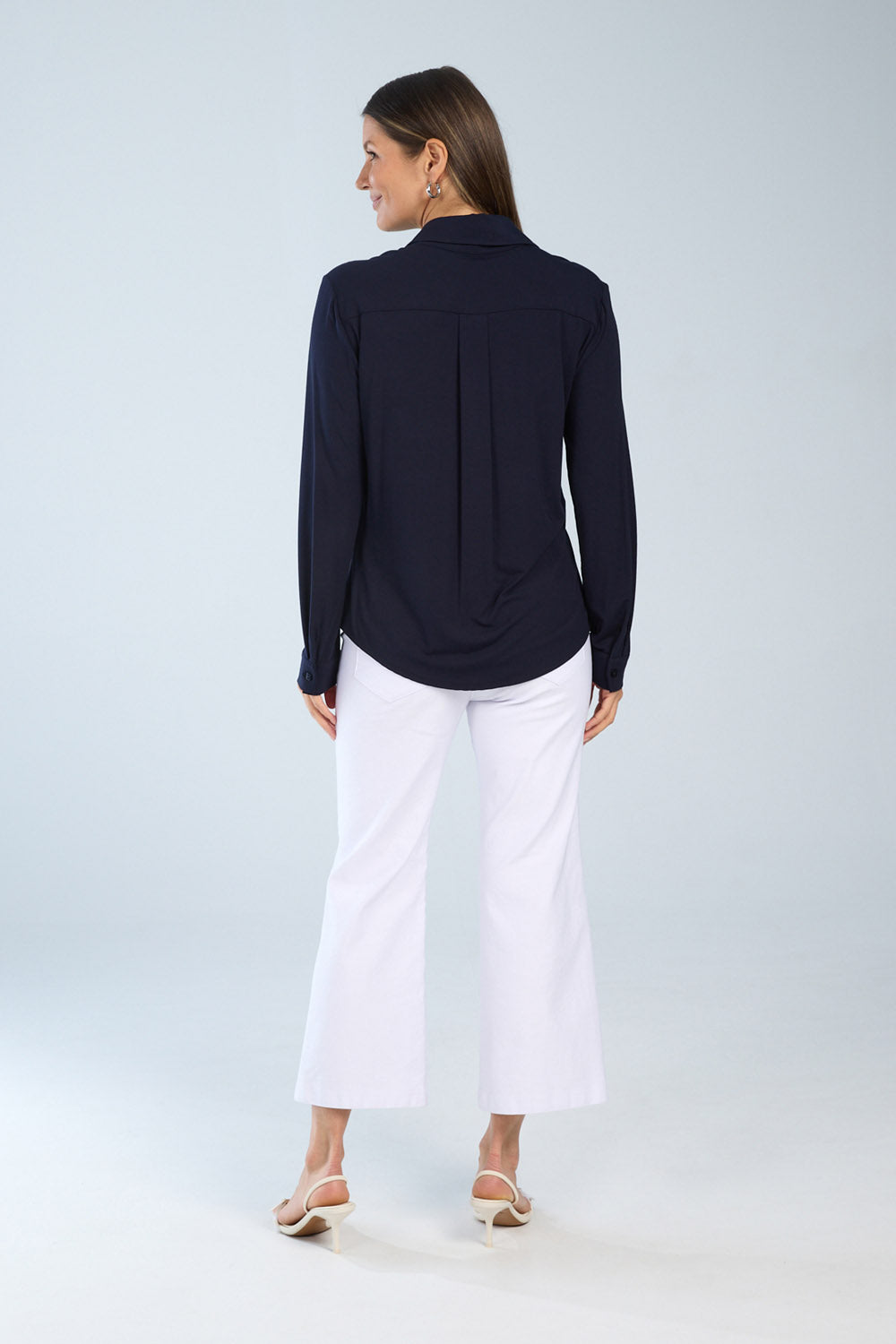 Woman wearing a navy blue blouse and white pants on a light gray background