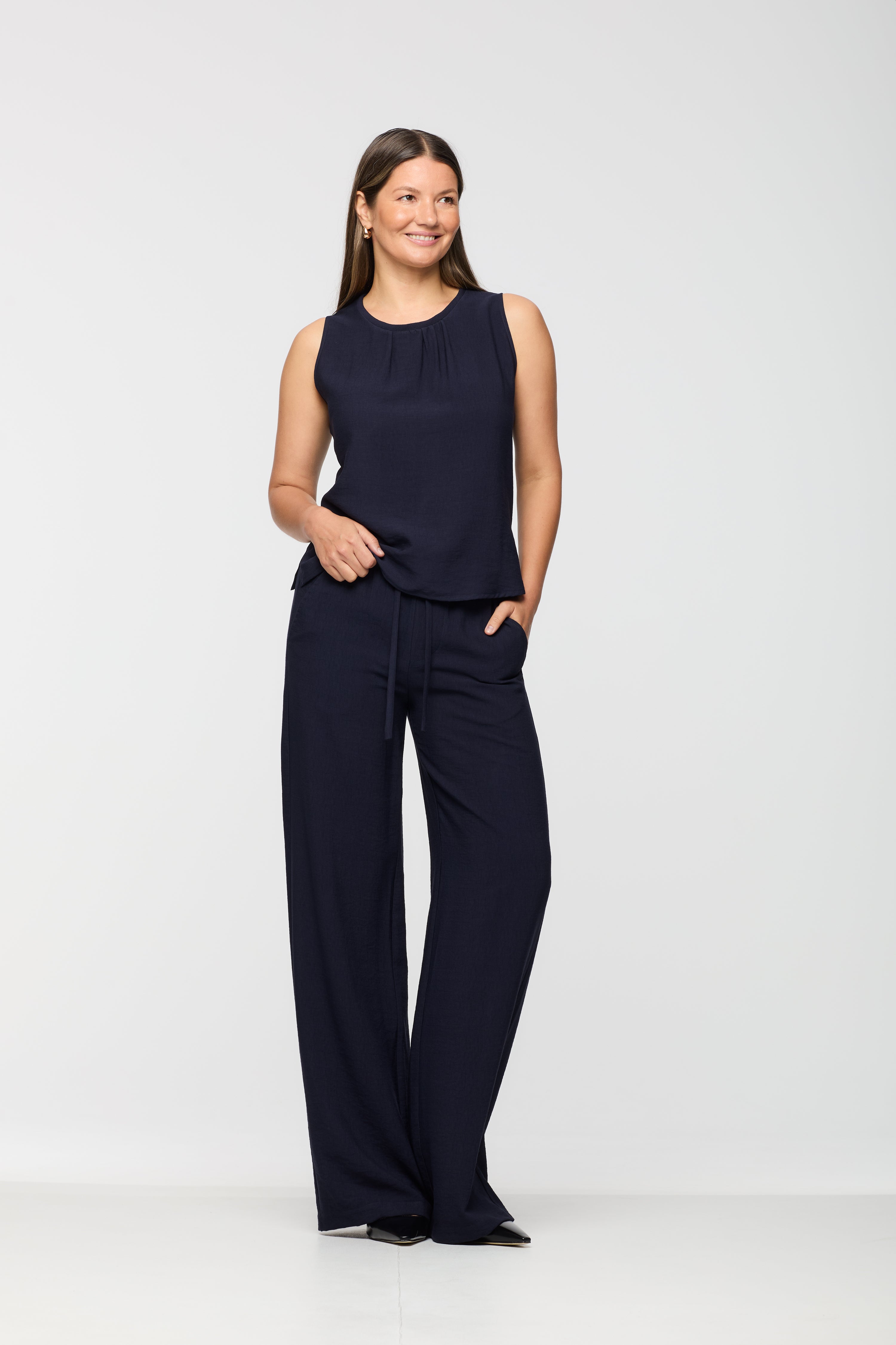 Woman wearing a sleeveless navy top with a round neckline and subtle pleat detail, paired with matching navy wide leg pants with an elastic waistband and drawstring.