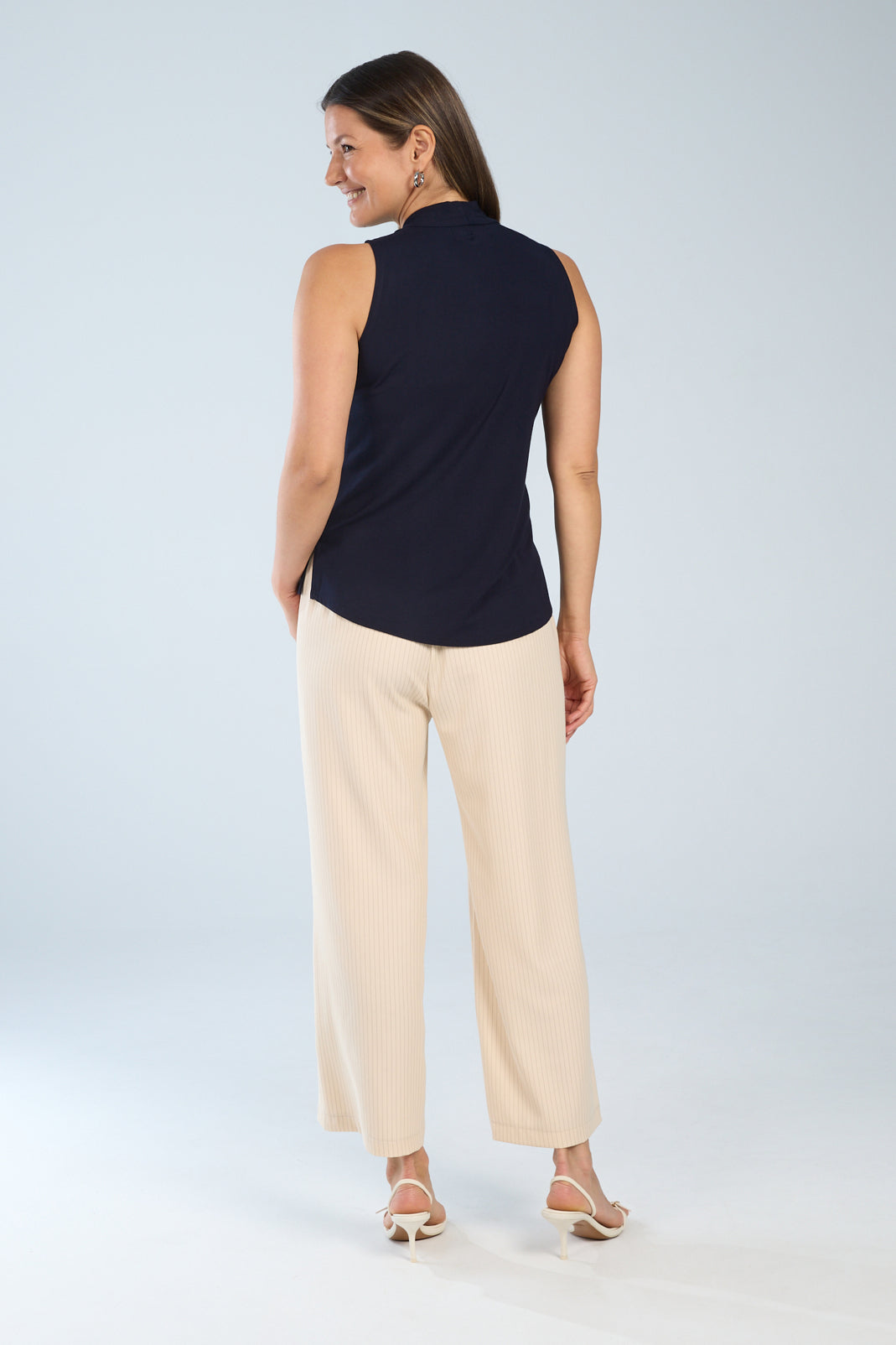 Woman wearing a sleeveless navy top shown from the back, featuring a relaxed fit and straight hem, paired with light beige straight leg pants.