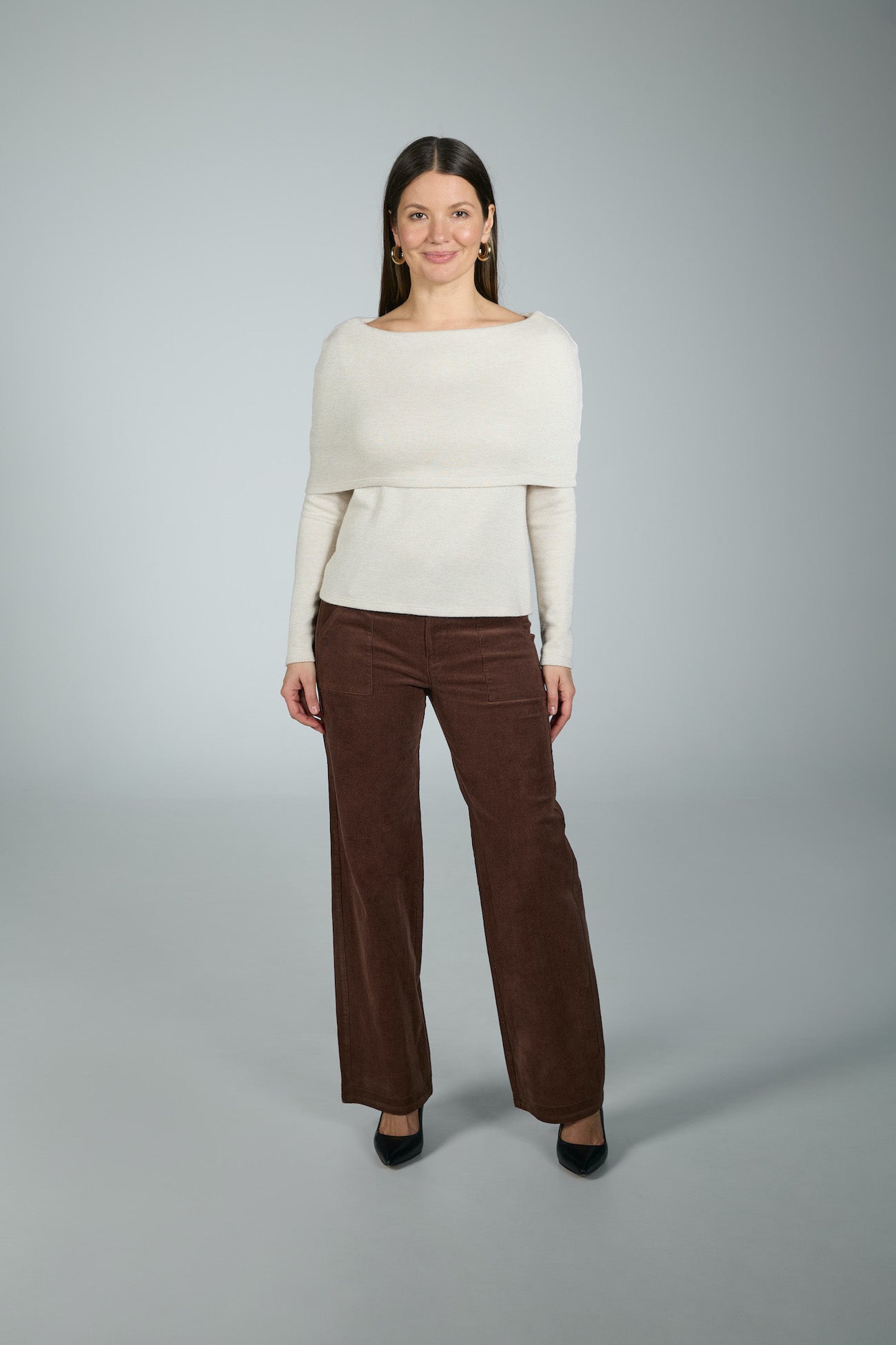 Woman wearing a white sweater and brown pants on a gray background