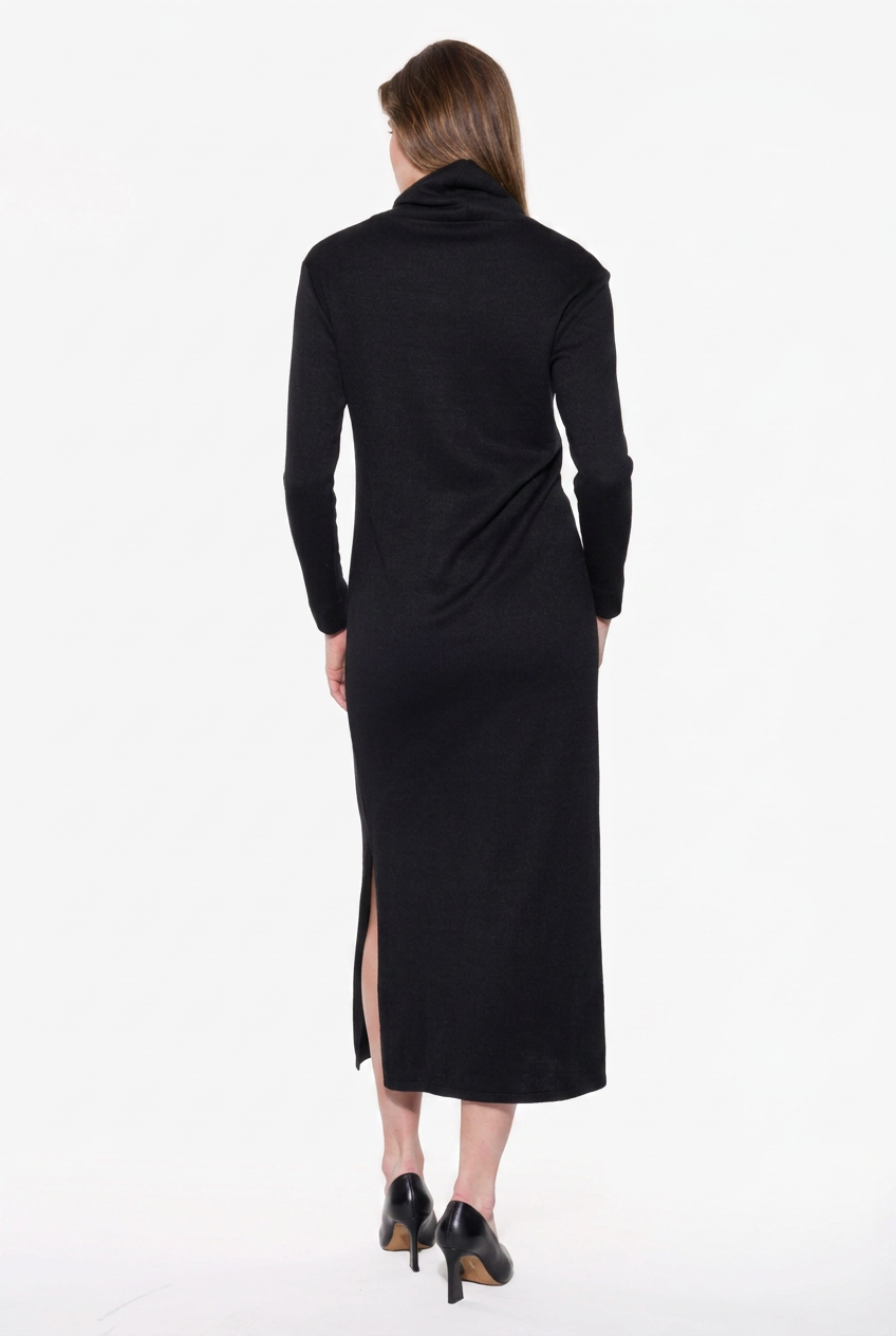 A woman viewed from the back wearing a long black cowl-neck midi dress with long sleeves and side slits, paired with black heels, against a plain white studio background.