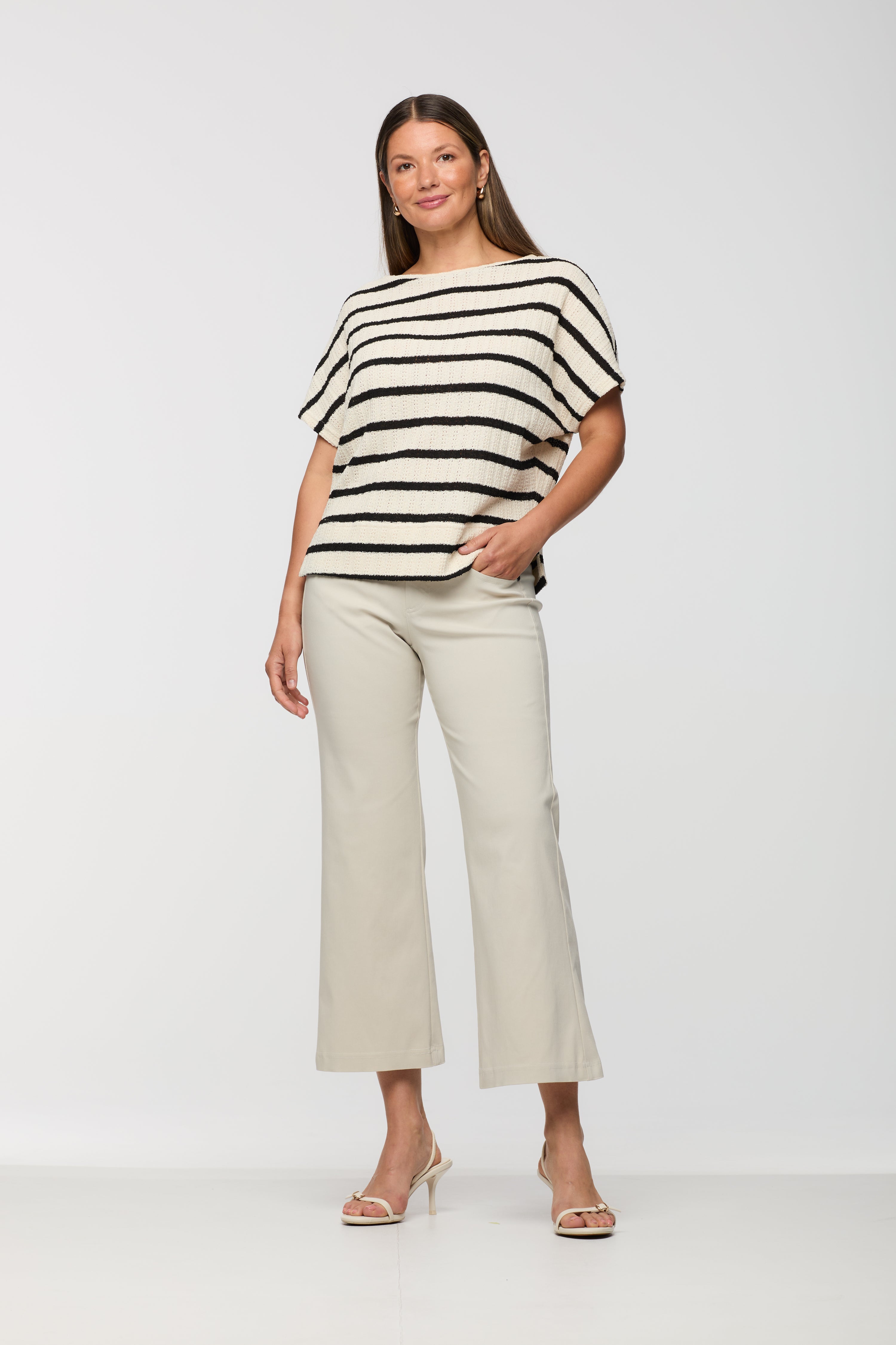 Woman wearing a short sleeve cream textured knit top with black horizontal stripes and a relaxed fit, paired with light beige cropped straight leg pants.