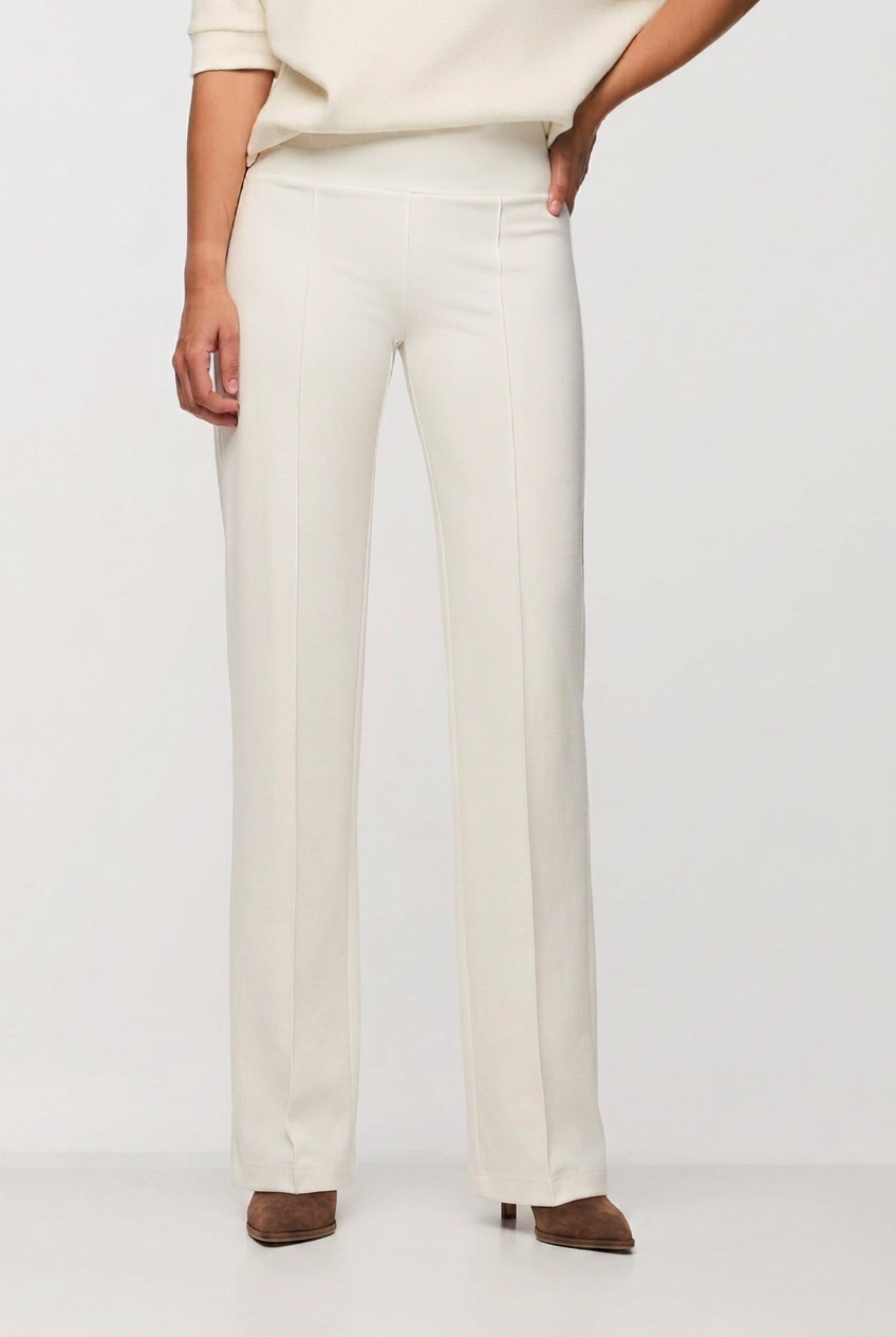 A model wearing a pair of off-white wide-leg trousers with a cream top and brown pointed-toe heels, shown from the waist down against a plain white studio background.