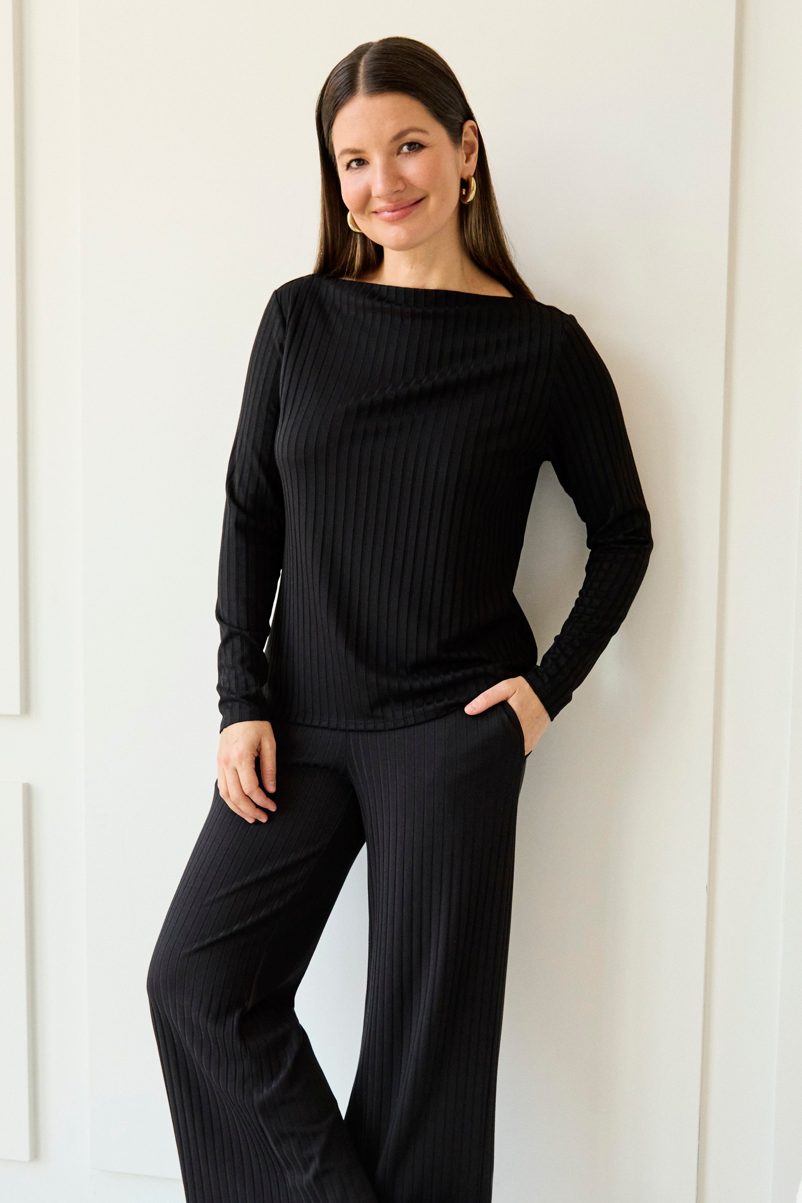 Woman wearing a black outfit standing against a white wall.