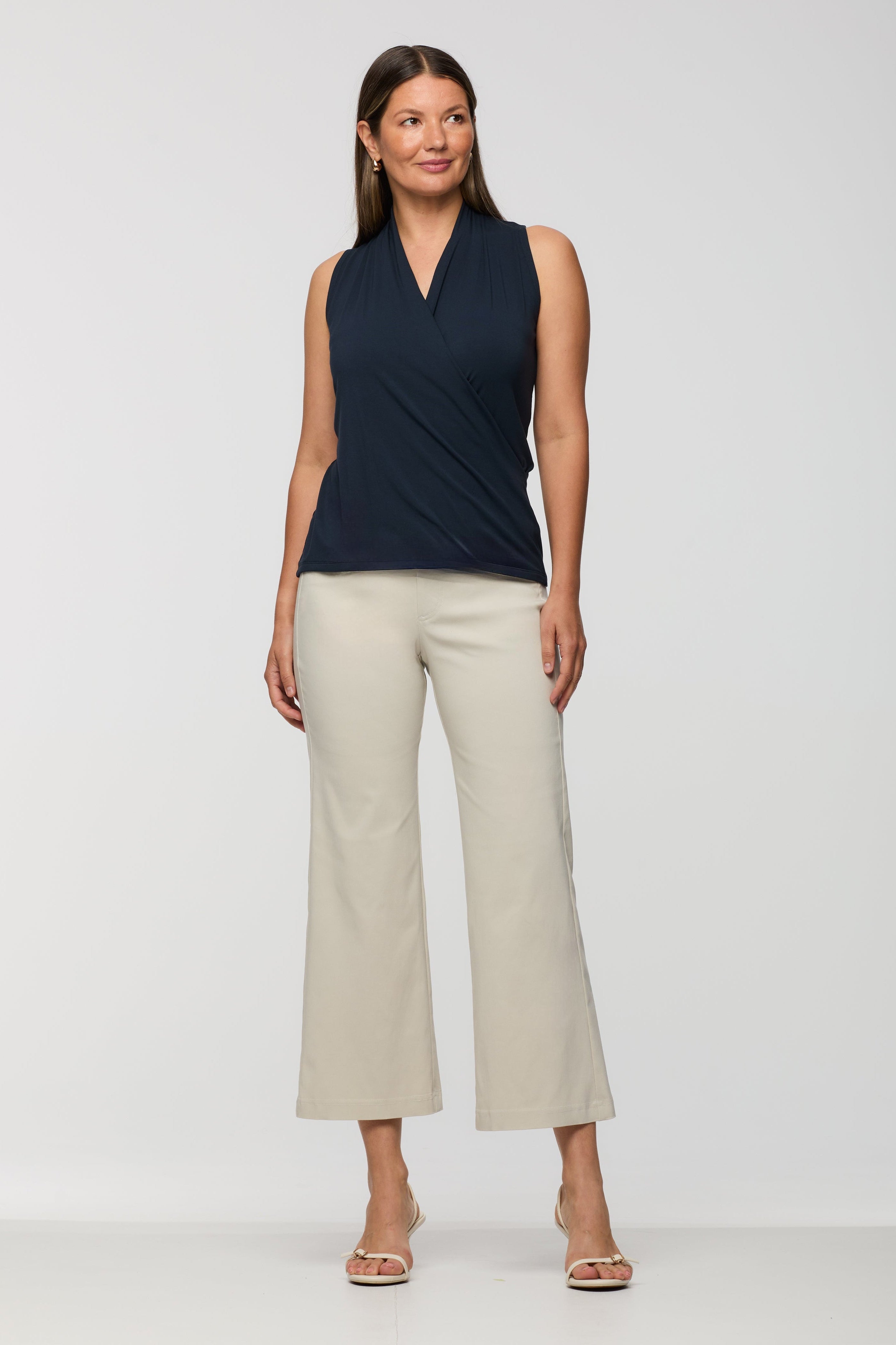 Woman wearing a sleeveless navy wrap-style top with a V-neckline and soft drape, paired with light beige cropped straight leg pants.