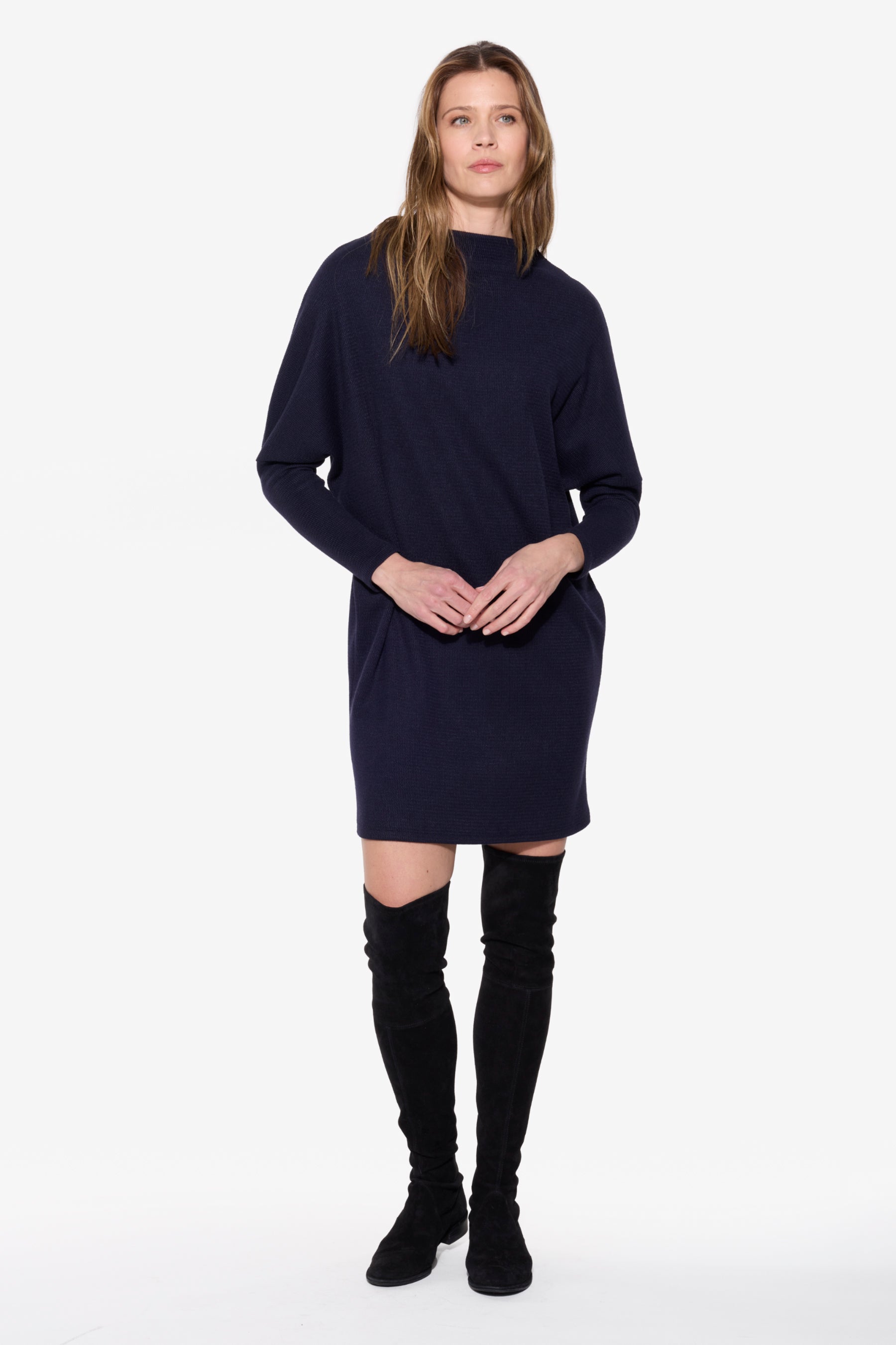 Woman wearing a navy blue dress with black knee-high boots on a white background