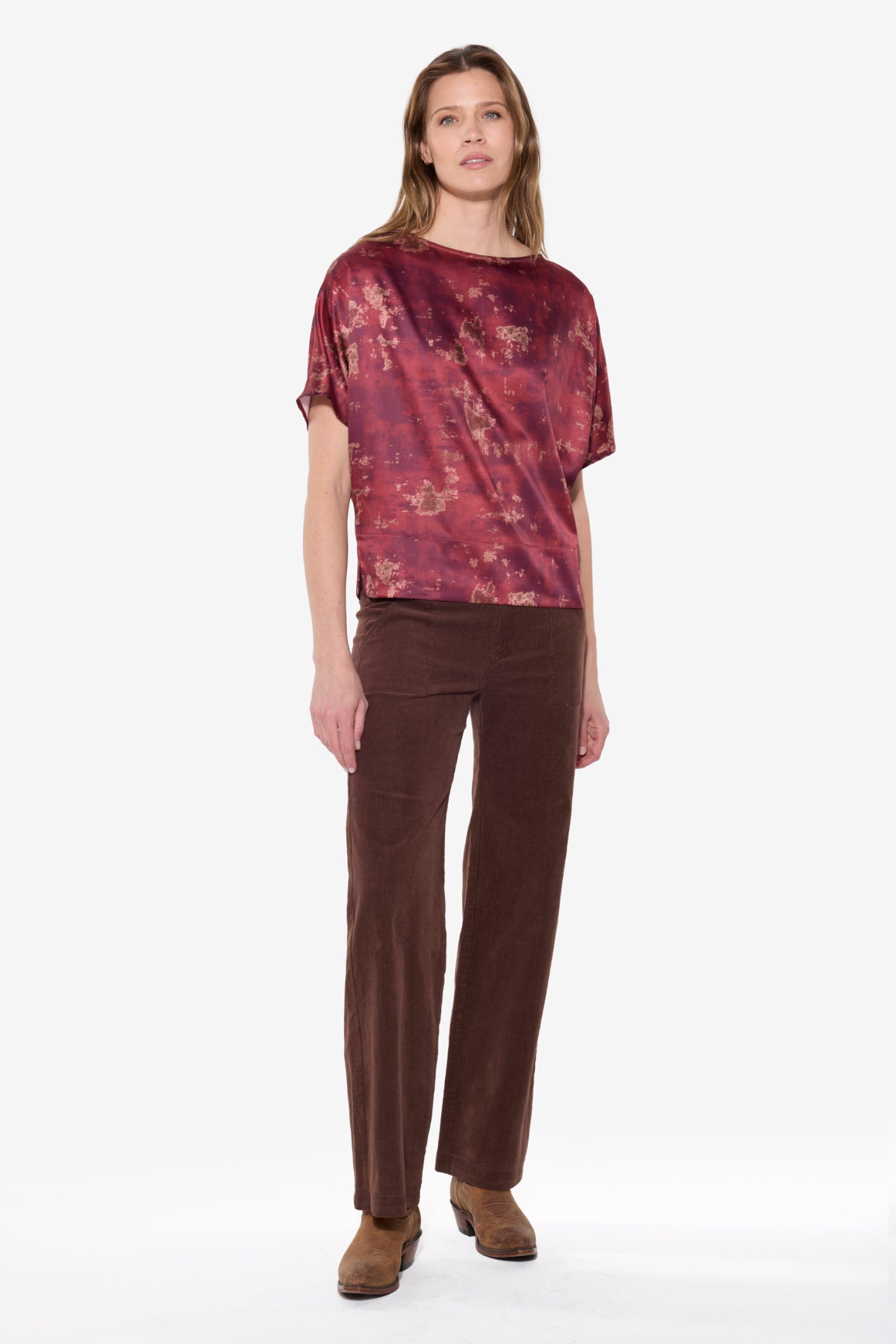 Woman wearing a patterned top and brown pants on a white background