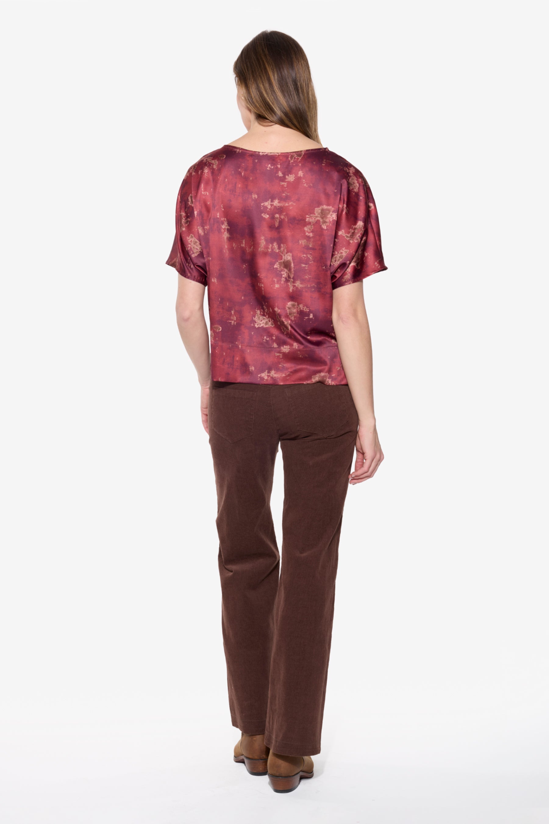 Back view of woman wearing a patterned top and brown pants on a white background