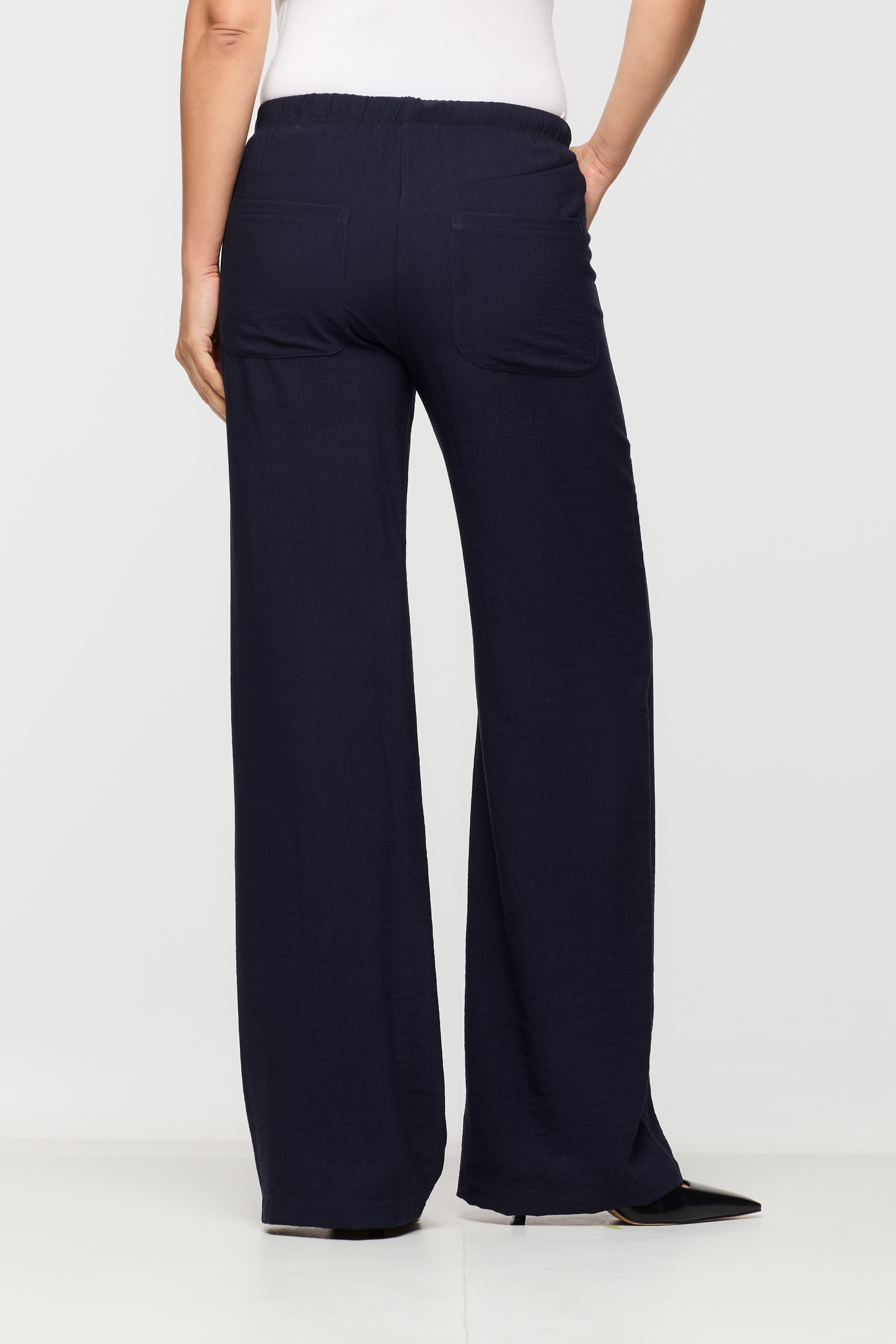 Woman wearing navy wide leg pants shown from the back, featuring an elastic waistband, relaxed fit, and back patch pockets.