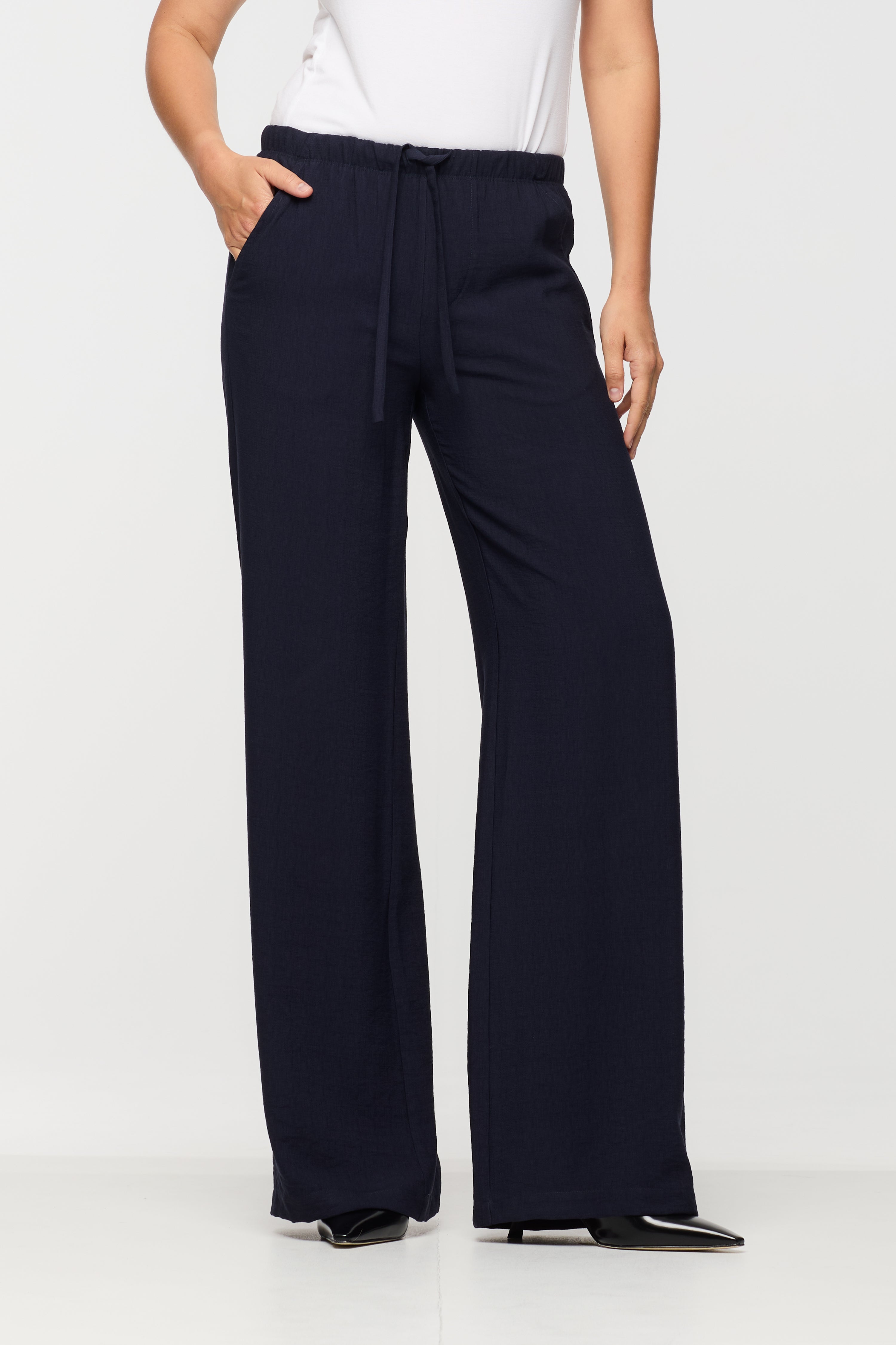 Woman wearing navy wide leg pants with an elastic waistband, adjustable drawstring, and front pockets, shown from the front.