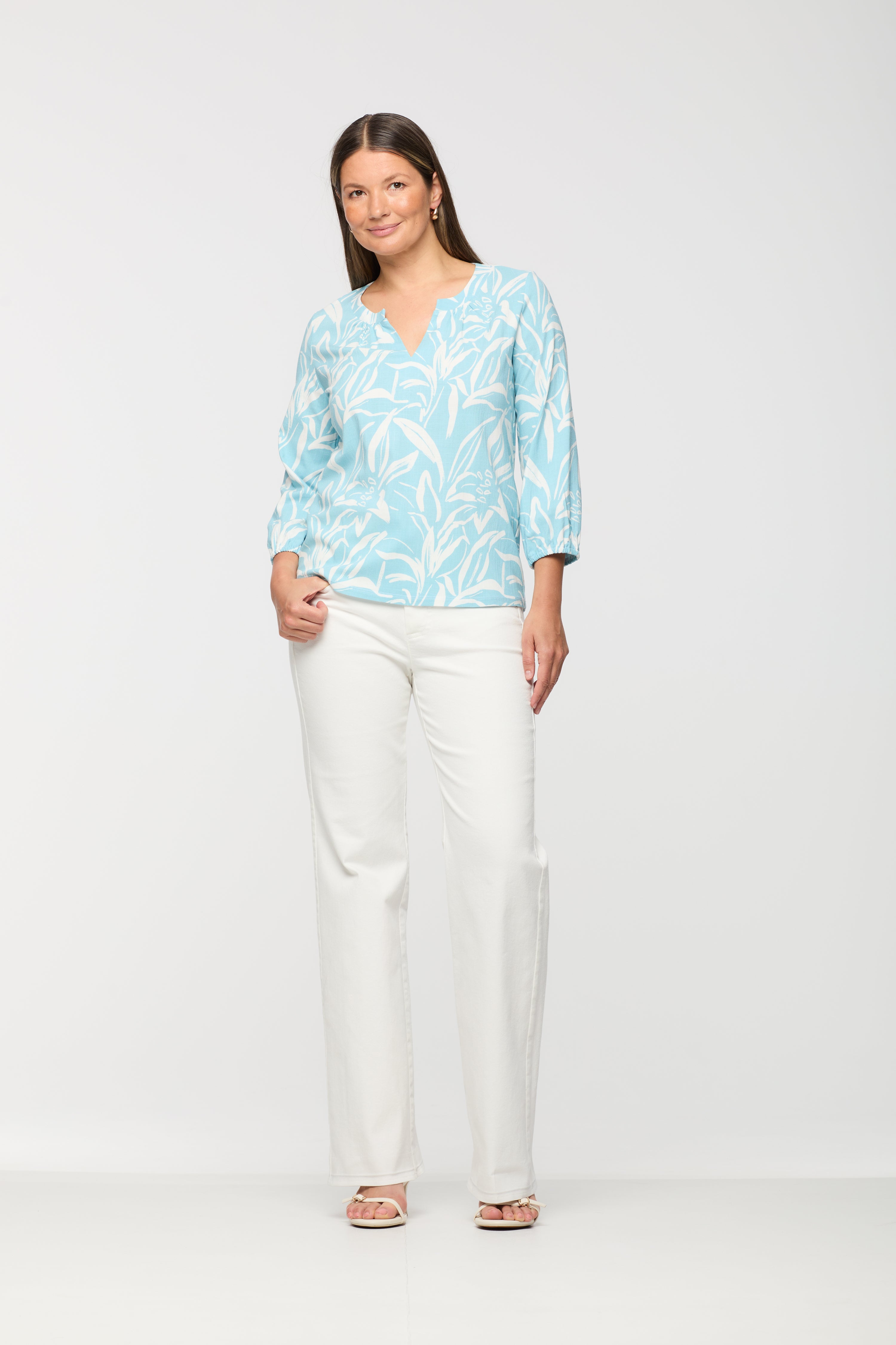 Woman wearing a light blue and white printed long sleeve top with a split neckline, relaxed fit, and straight hem, paired with white straight leg pants.