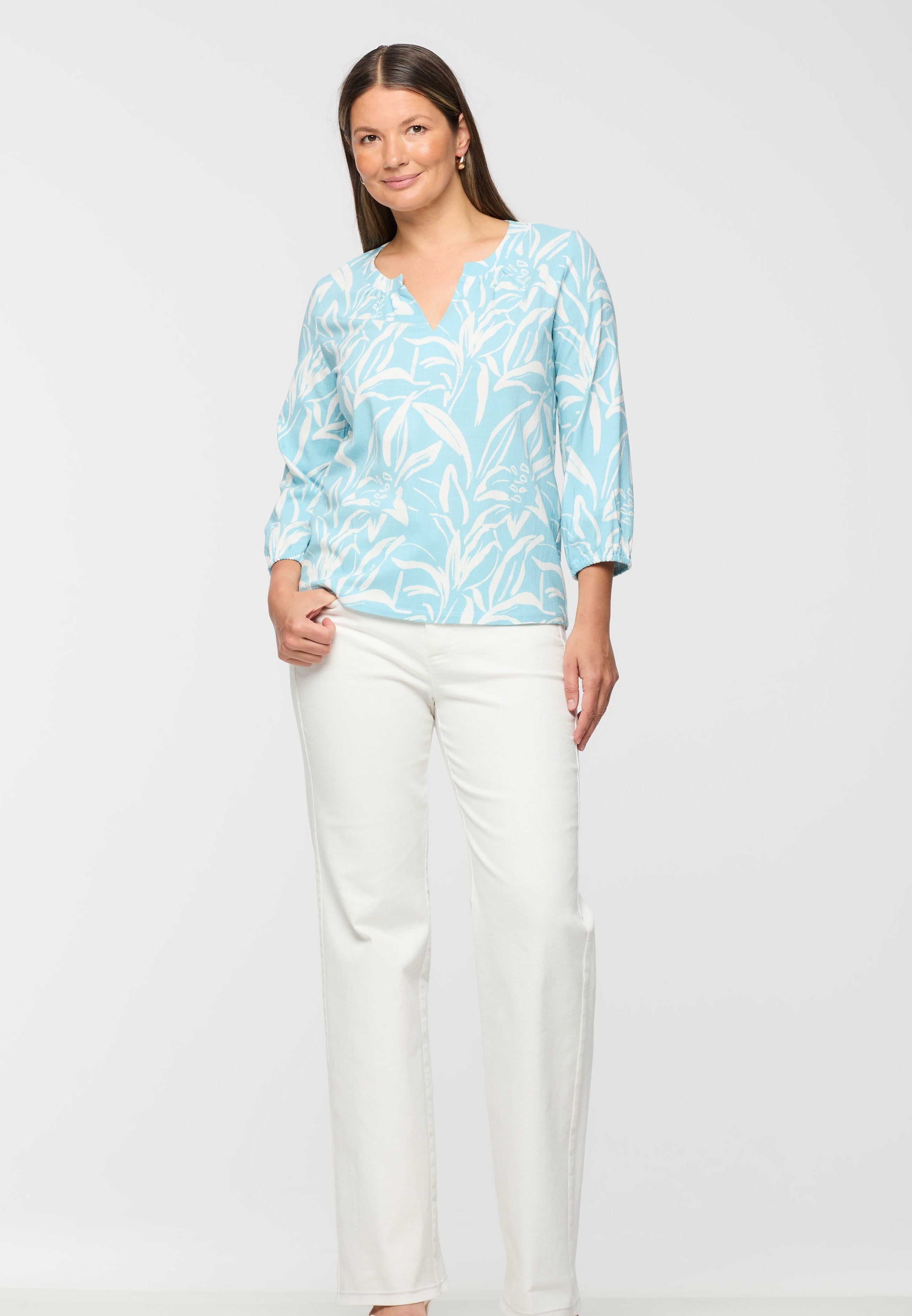 Woman wearing a light blue patterned blouse and white pants on a white background