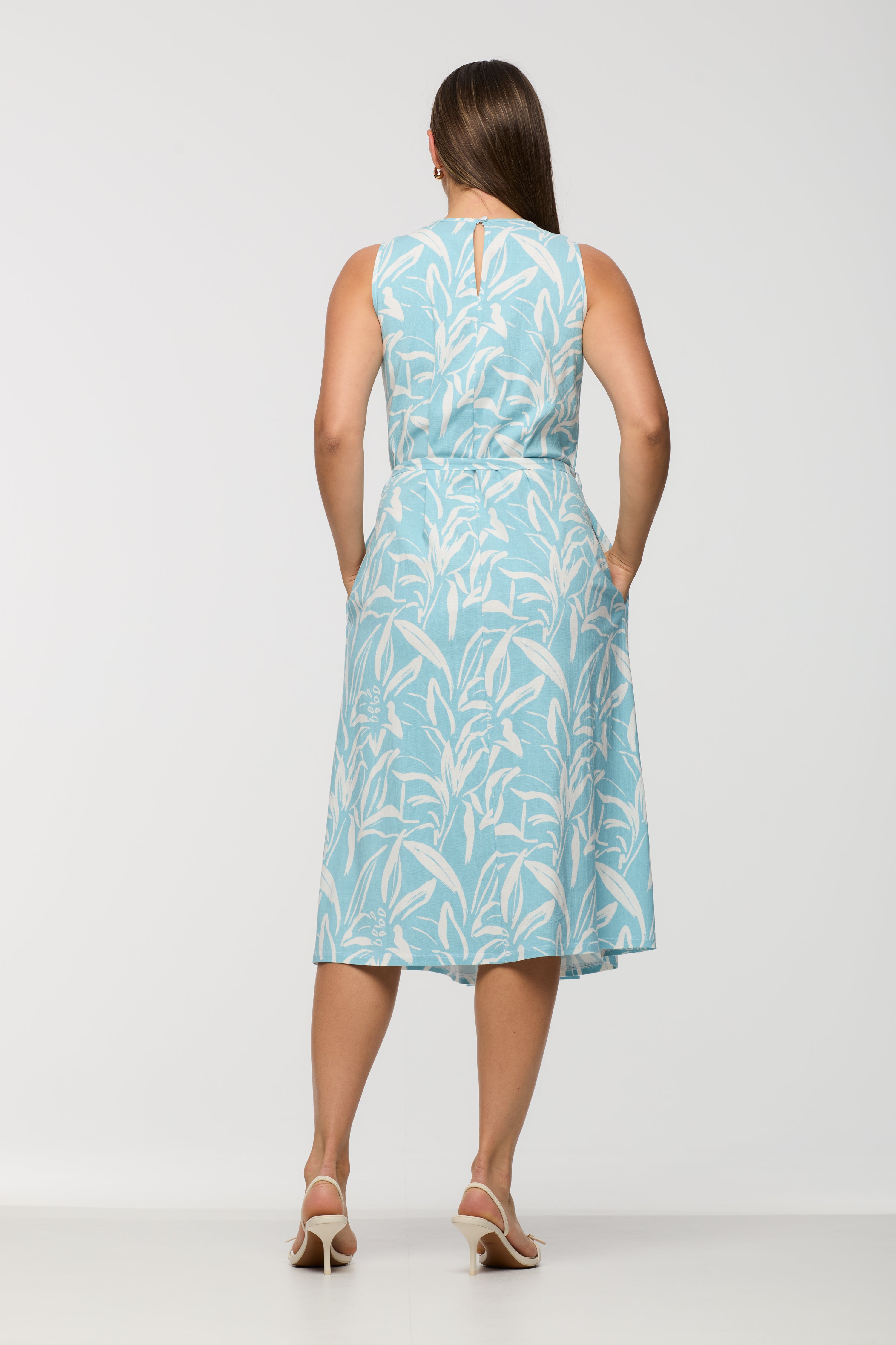 Woman wearing a sleeveless light blue and white printed midi dress shown from the back, featuring a keyhole neckline, fitted waist with self-tie belt, and relaxed skirt.