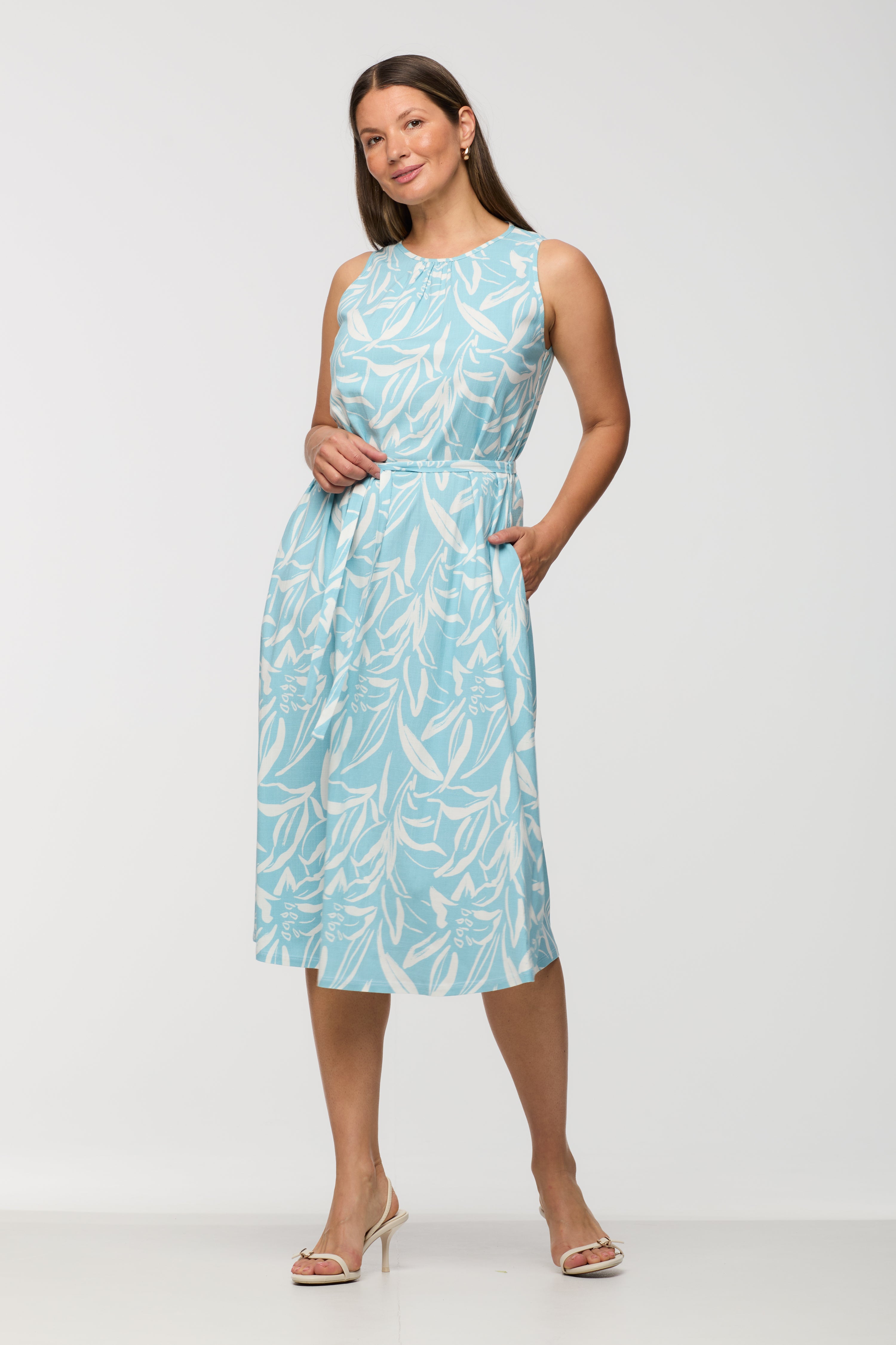 Woman wearing a sleeveless light blue and white printed midi dress with a round neckline, fitted waist with self-tie belt, and relaxed skirt, shown from the front.
