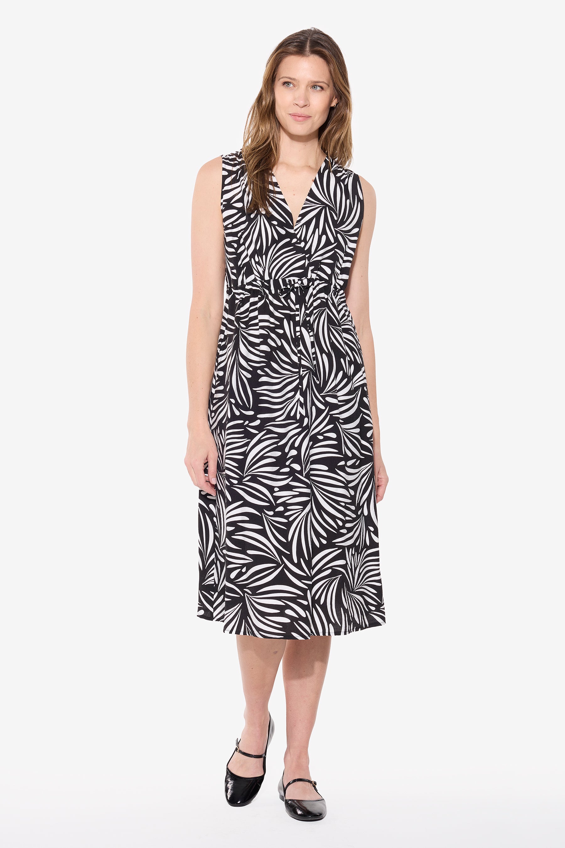Woman wearing a black and white printed sleeveless dress with V neckline, adjustable waist tie and knee-length silhouette