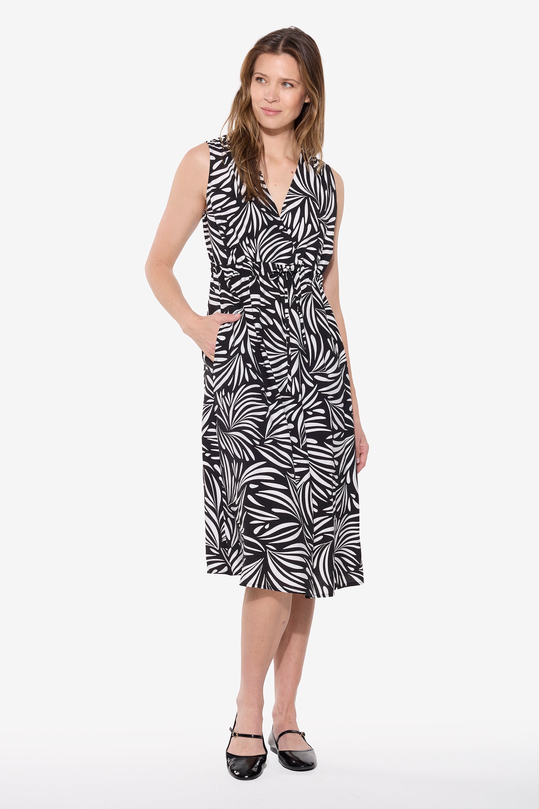 Woman wearing a black and white abstract print sleeveless dress with V neckline, adjustable drawstring waist and side pockets