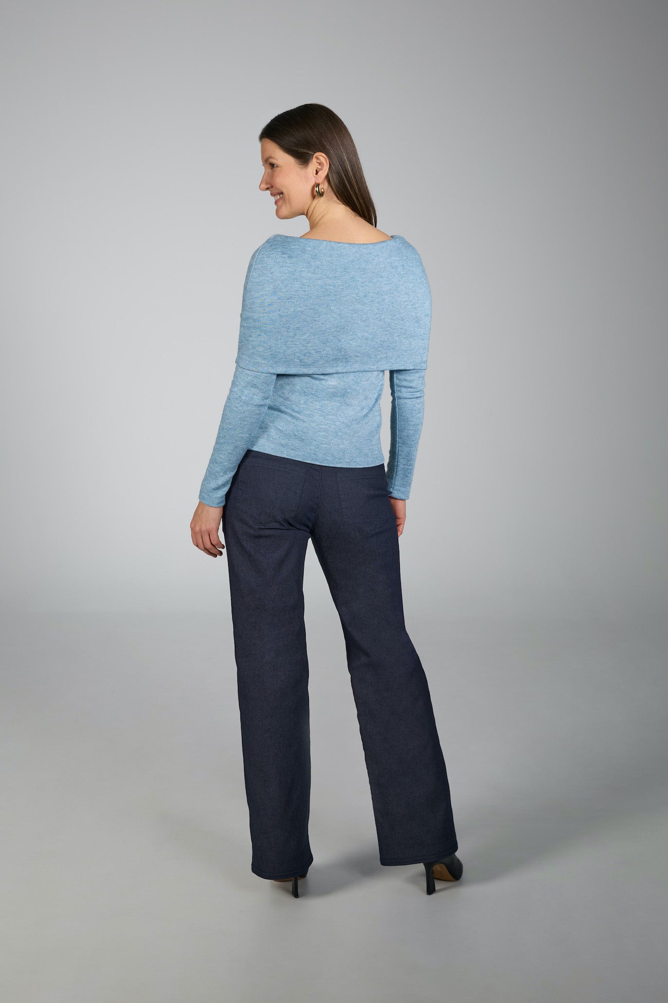 Woman wearing a light blue sweater and dark blue pants on a gray background