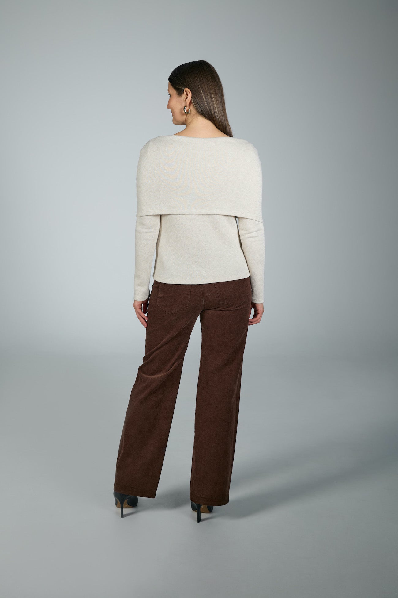 Woman wearing a white sweater and brown pants on a gray background