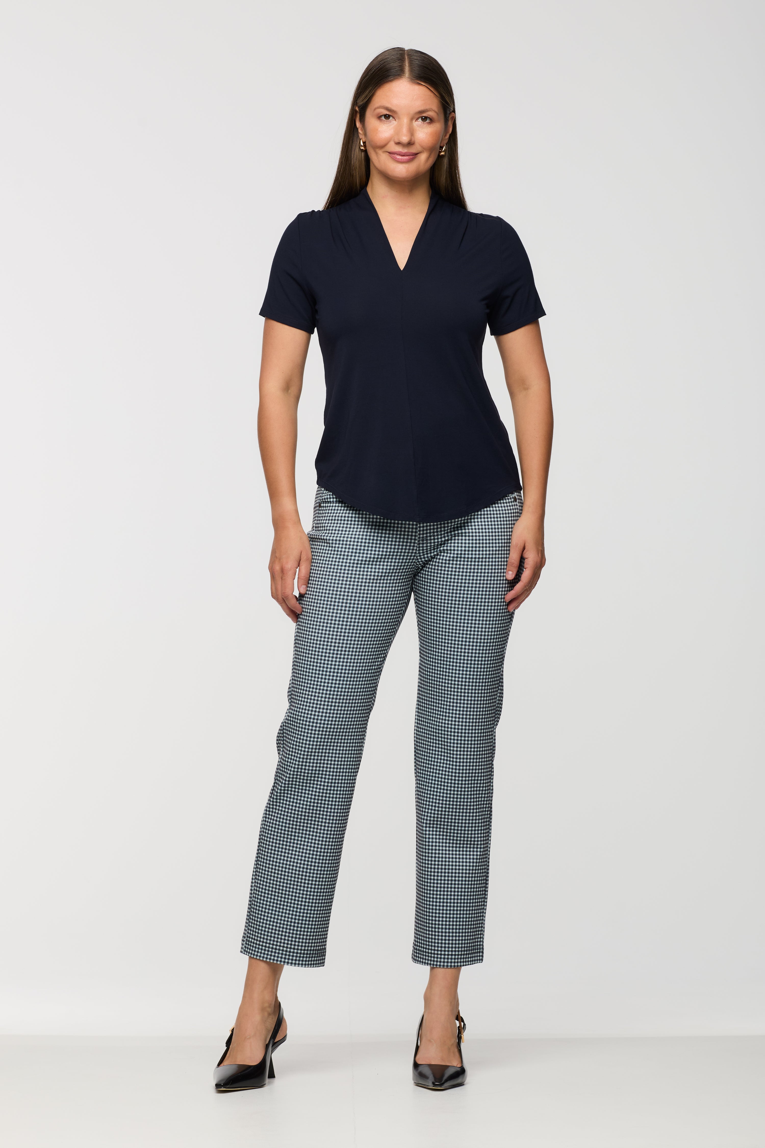 Woman wearing a short sleeve navy top with a V-neckline and curved hem, paired with black and white check cropped straight leg pants.