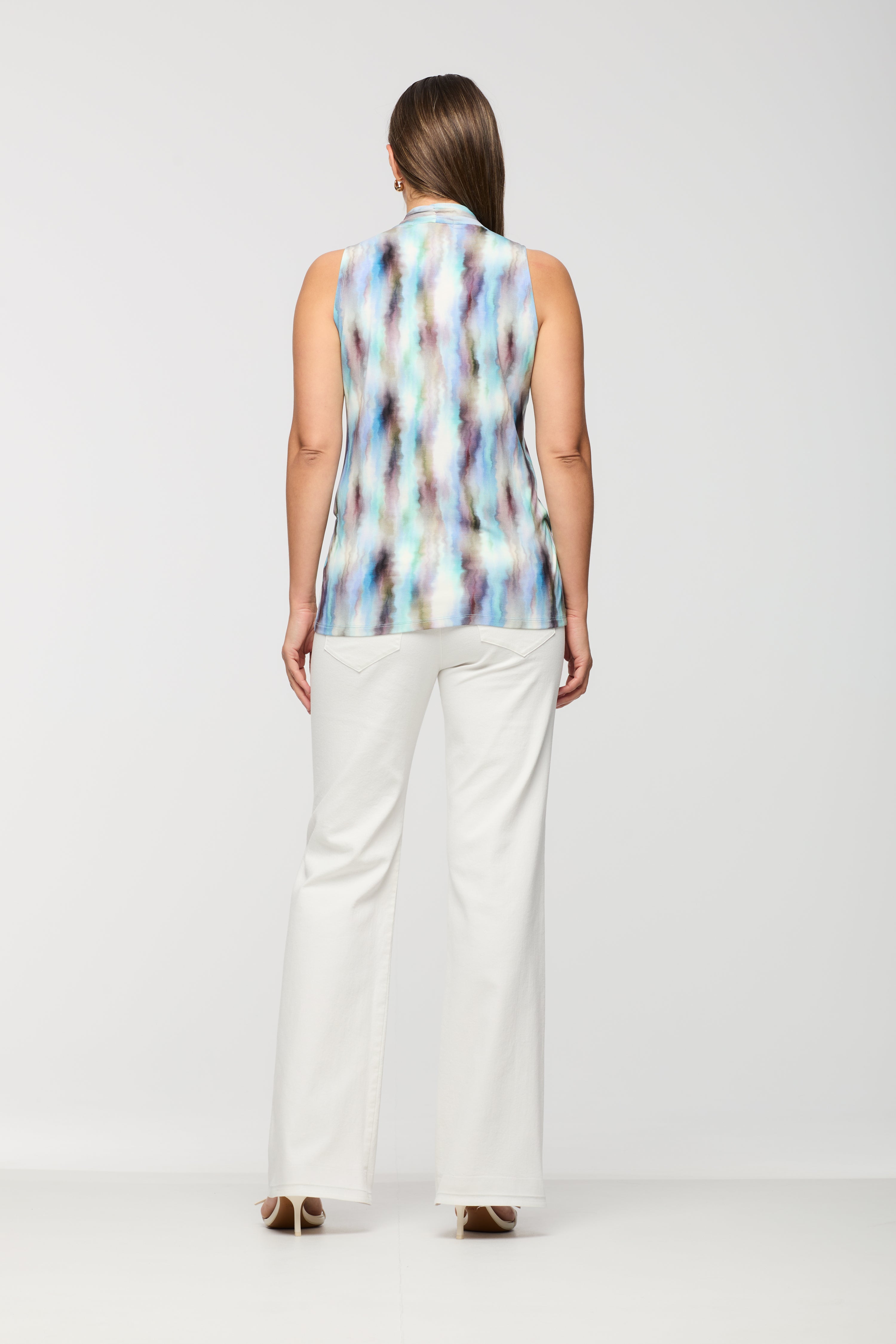Woman wearing a sleeveless printed wrap-style top shown from the back, featuring a relaxed fit and straight hem, paired with white straight leg pants.