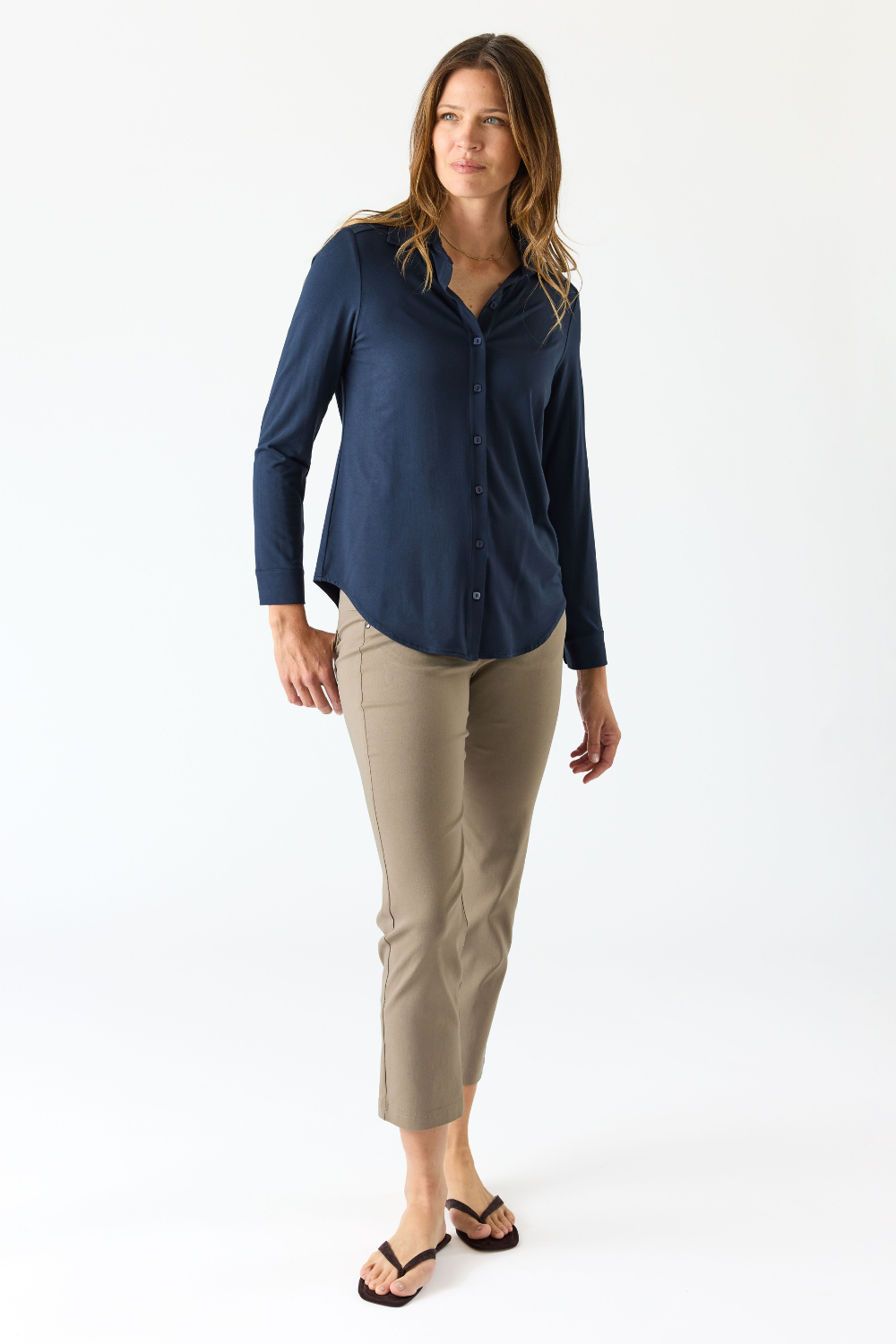 A woman modeling a navy blue long-sleeve button-up shirt and beige cropped pants against a plain white studio background.