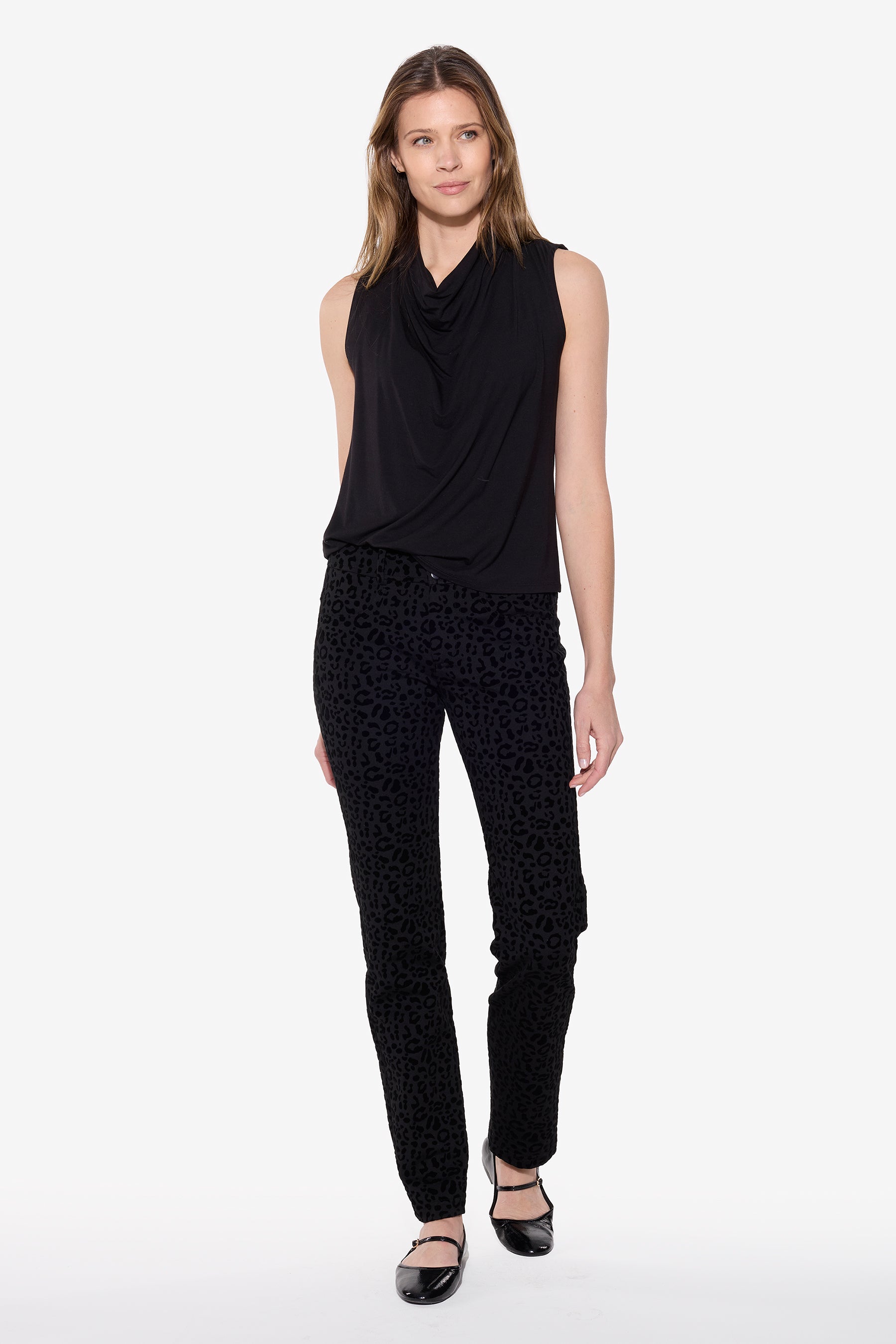 Woman wearing a black sleeveless top and patterned black pants on a white background