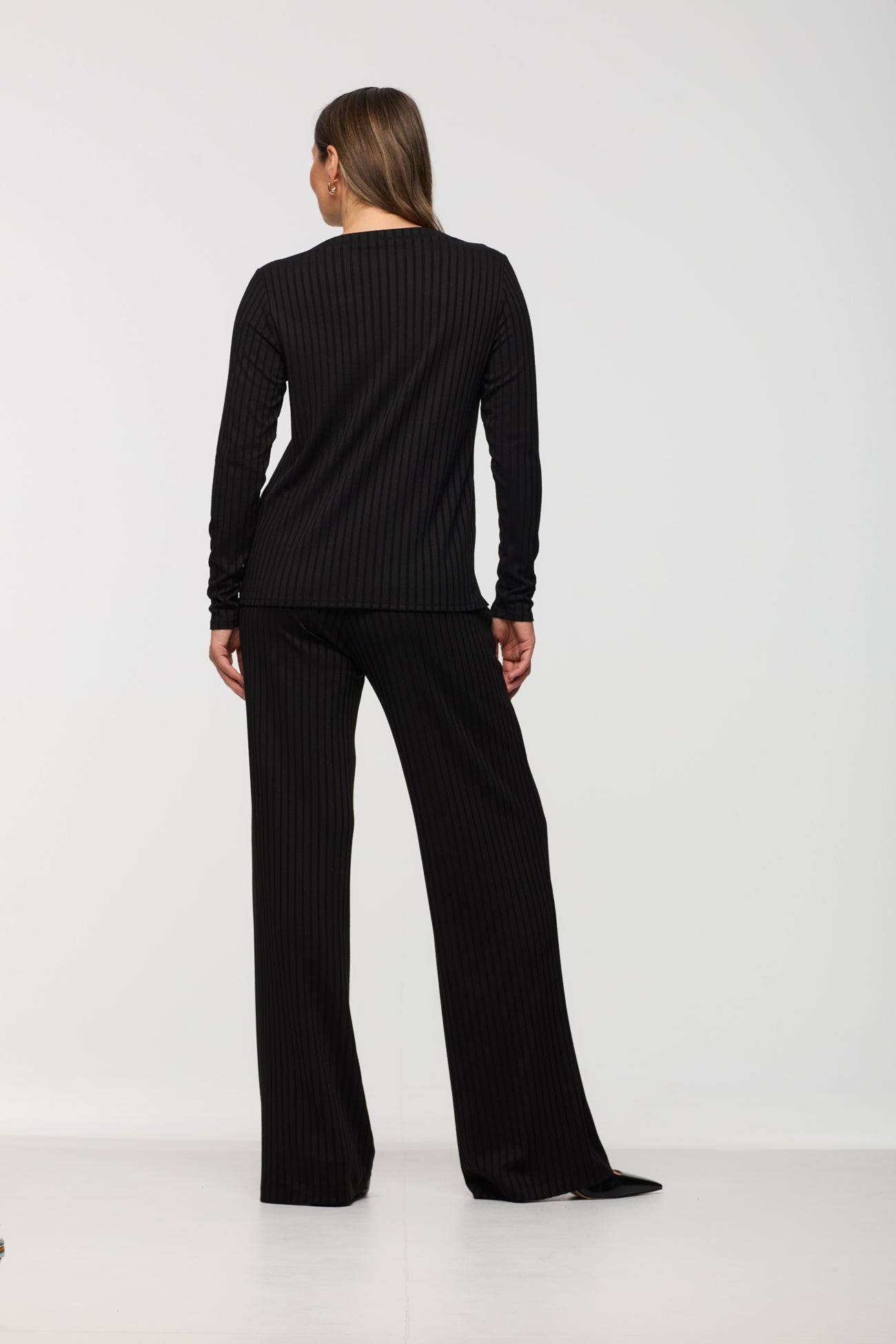 Person wearing a black ribbed long-sleeve top and black wide-leg pants on a white background