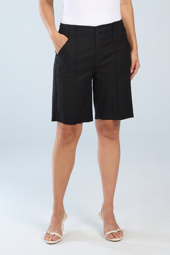 Woman wearing black linen bermuda shorts with a tailored fit, knee length hem, front pockets, and seam detailing, styled with a white top.
