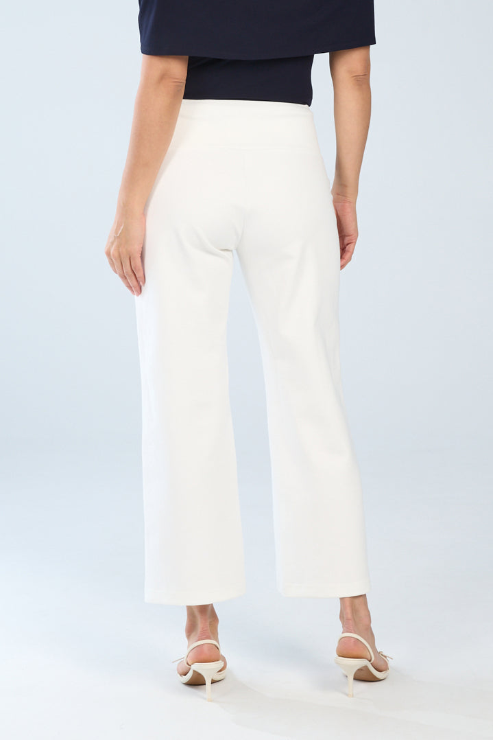 A model wearing white wide leg pintuck crop pants with a slimming effect, paired with a navy top and standing against a blue background back view