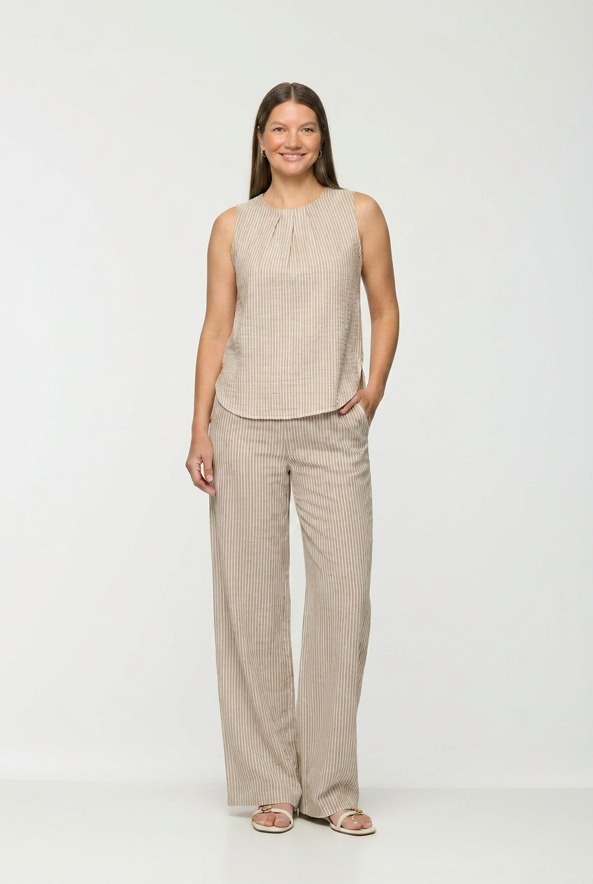 Woman wearing a beige sleeveless top and wide-leg pants on a white background