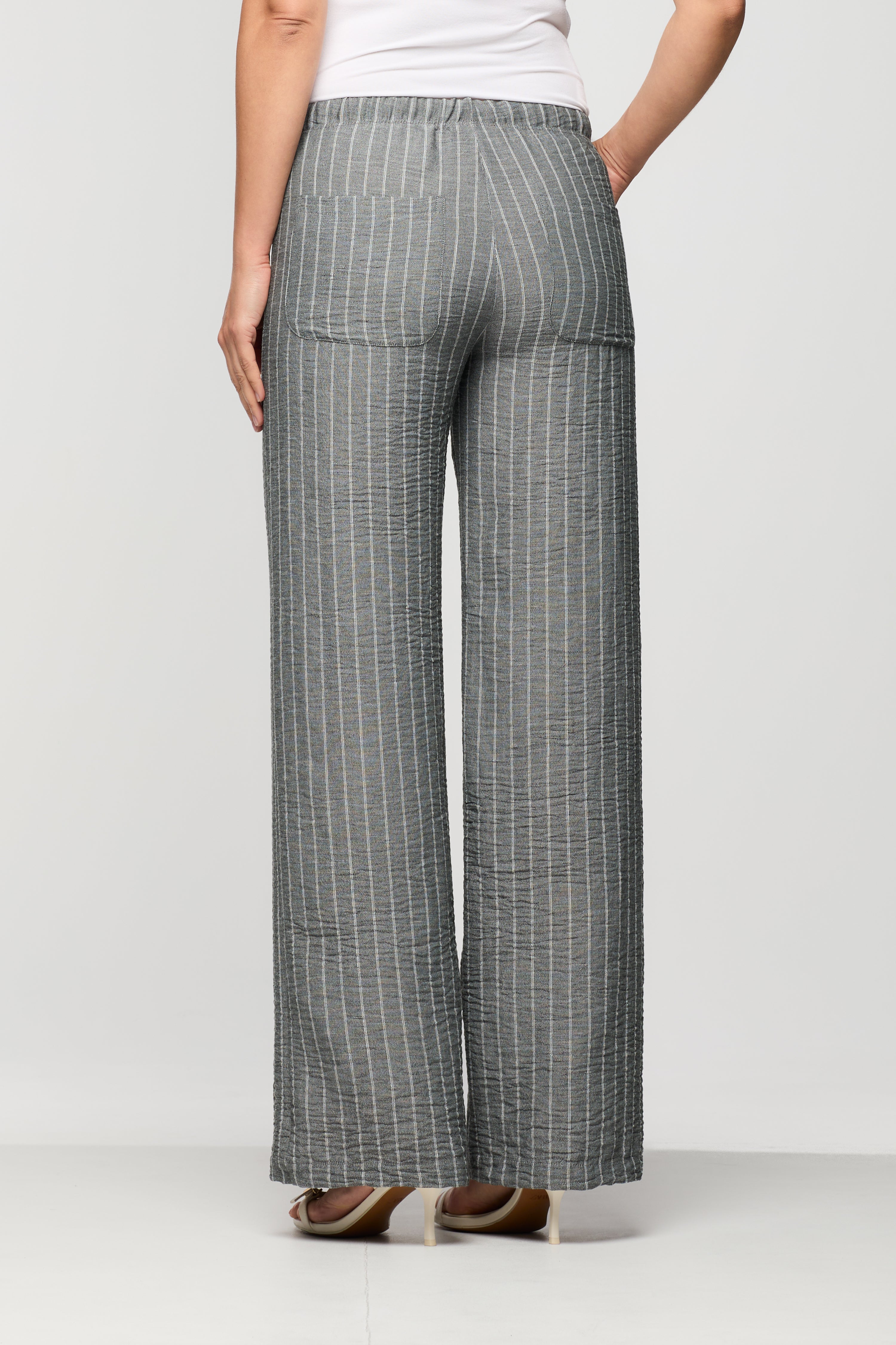 Woman wearing grey pinstripe wide leg pants shown from the back, featuring an elastic waistband and patch pockets.