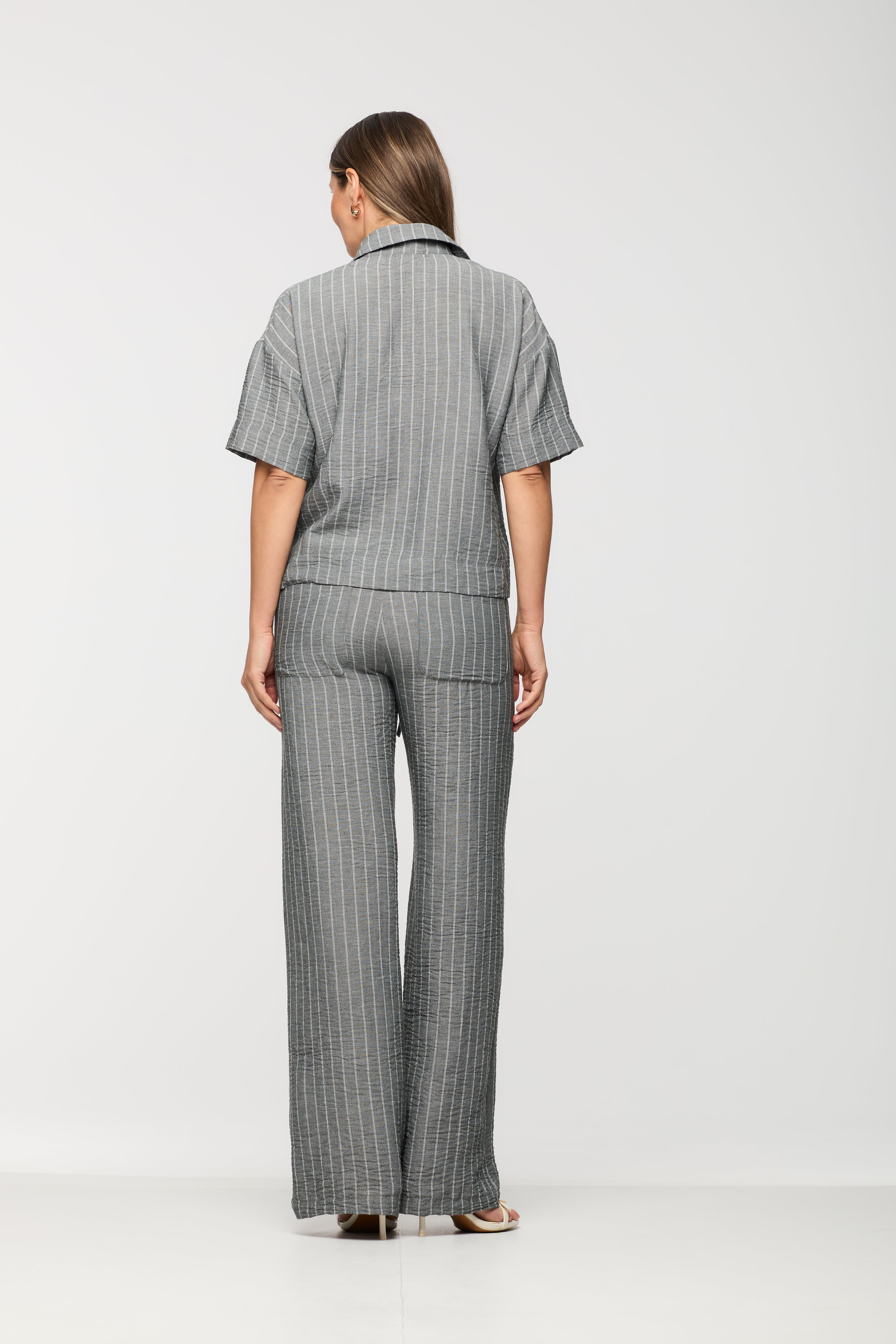 Woman wearing a grey pinstripe short sleeve shirt shown from the back, paired with matching wide leg drawstring pants.