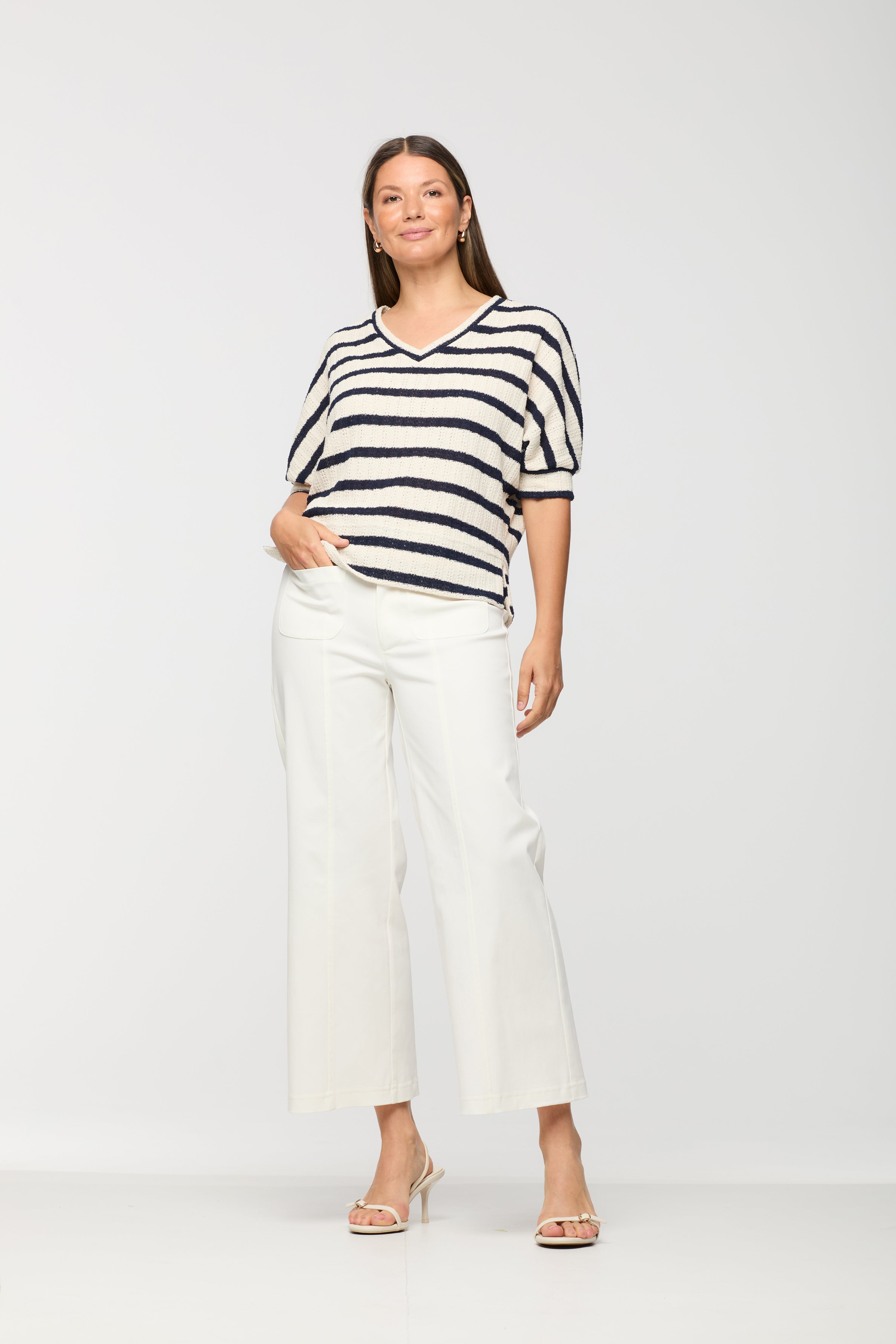 Woman wearing a short sleeve cream knit top with black horizontal stripes, V-neckline, and relaxed fit, paired with white wide leg cropped pants.