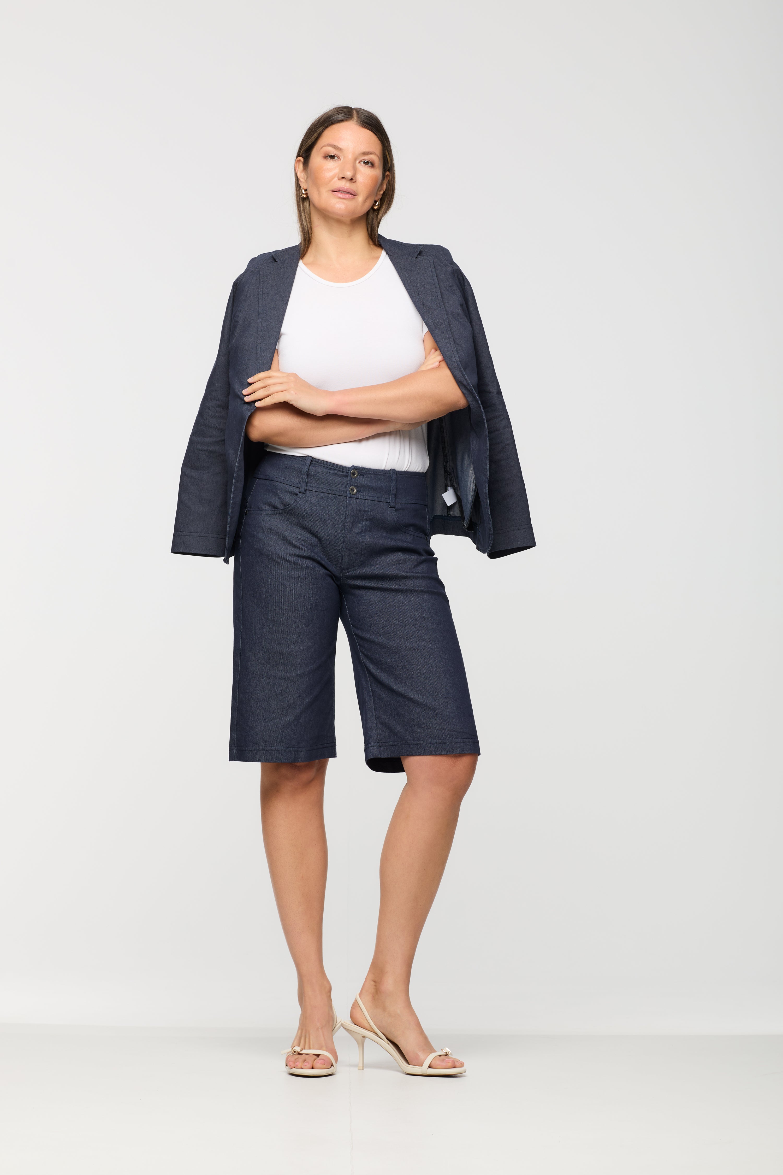 Woman wearing a navy blazer, white top, and navy shorts on a white background