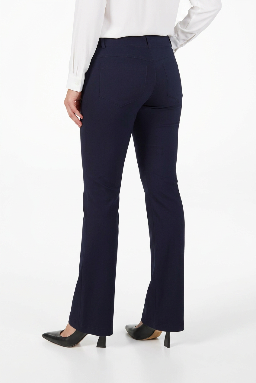 A model shown from the back wearing dark navy blue flared trousers, a white long-sleeve blouse, and black pointed-toe heels against a plain white studio background.