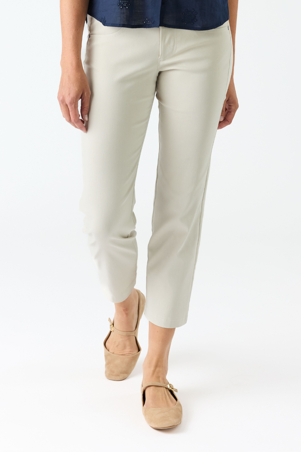 A person wearing off white cropped pants with a navy top and tan flat shoes, shown from the waist down against a plain white studio background.