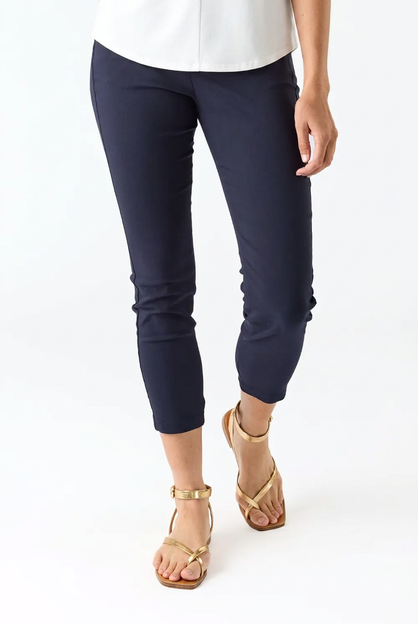 A person wearing navy cropped pants with gathered cuffs, paired with a white top and gold strappy sandals, shown against a plain white studio background.
