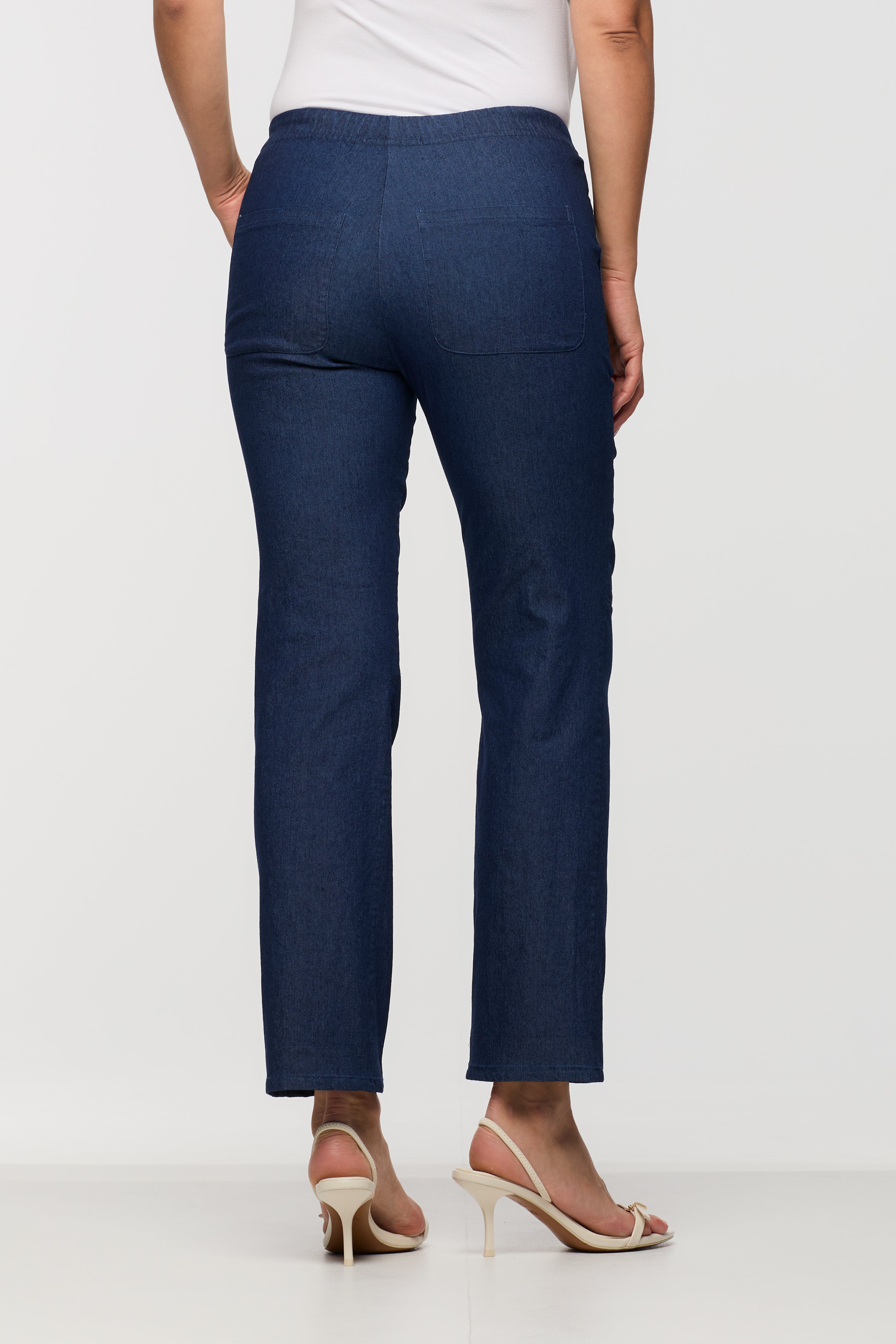 Woman wearing dark indigo drawstring straight leg pants shown from the back, featuring an elastic waistband and patch pockets.