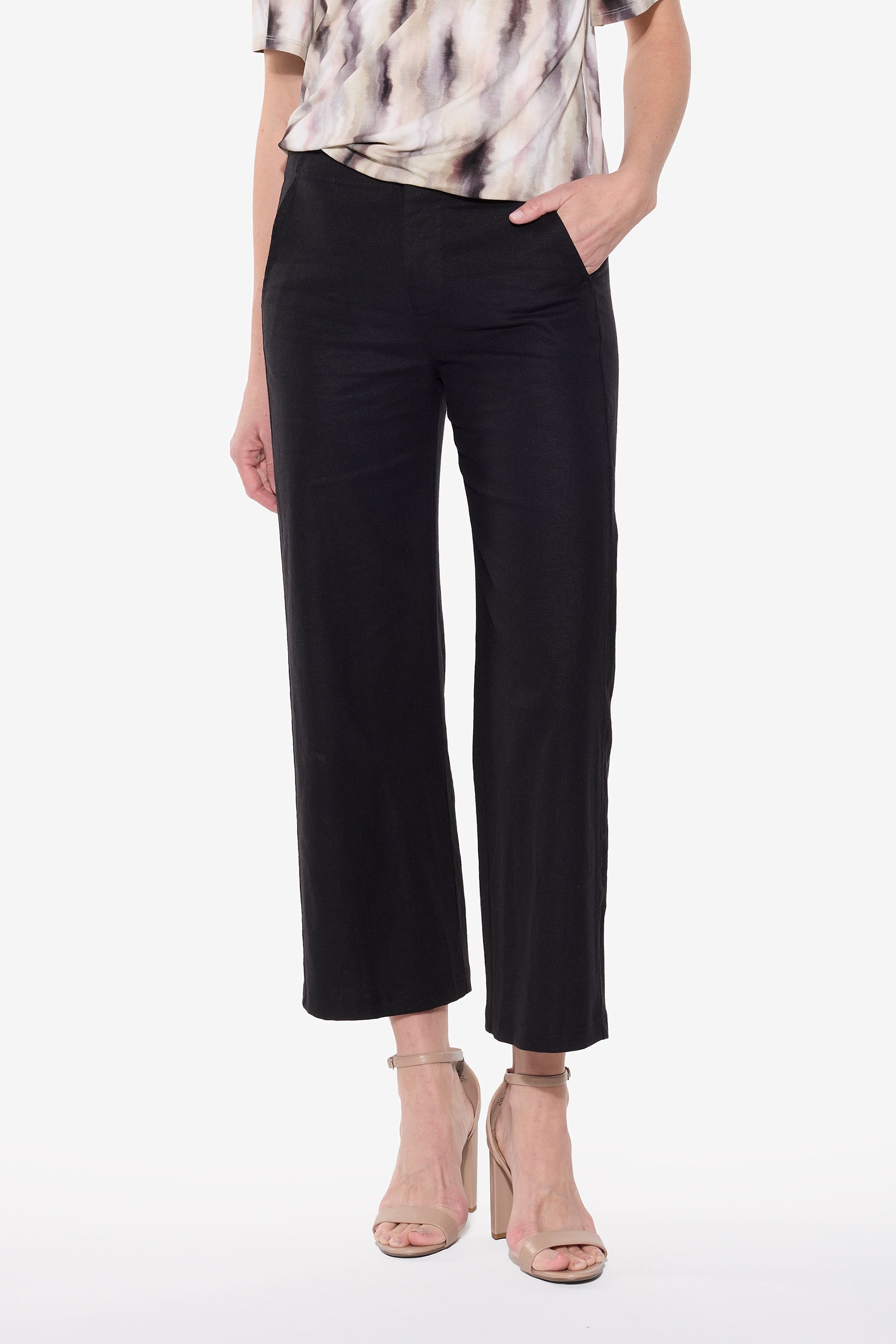 Person wearing black pants and a patterned top on a white background