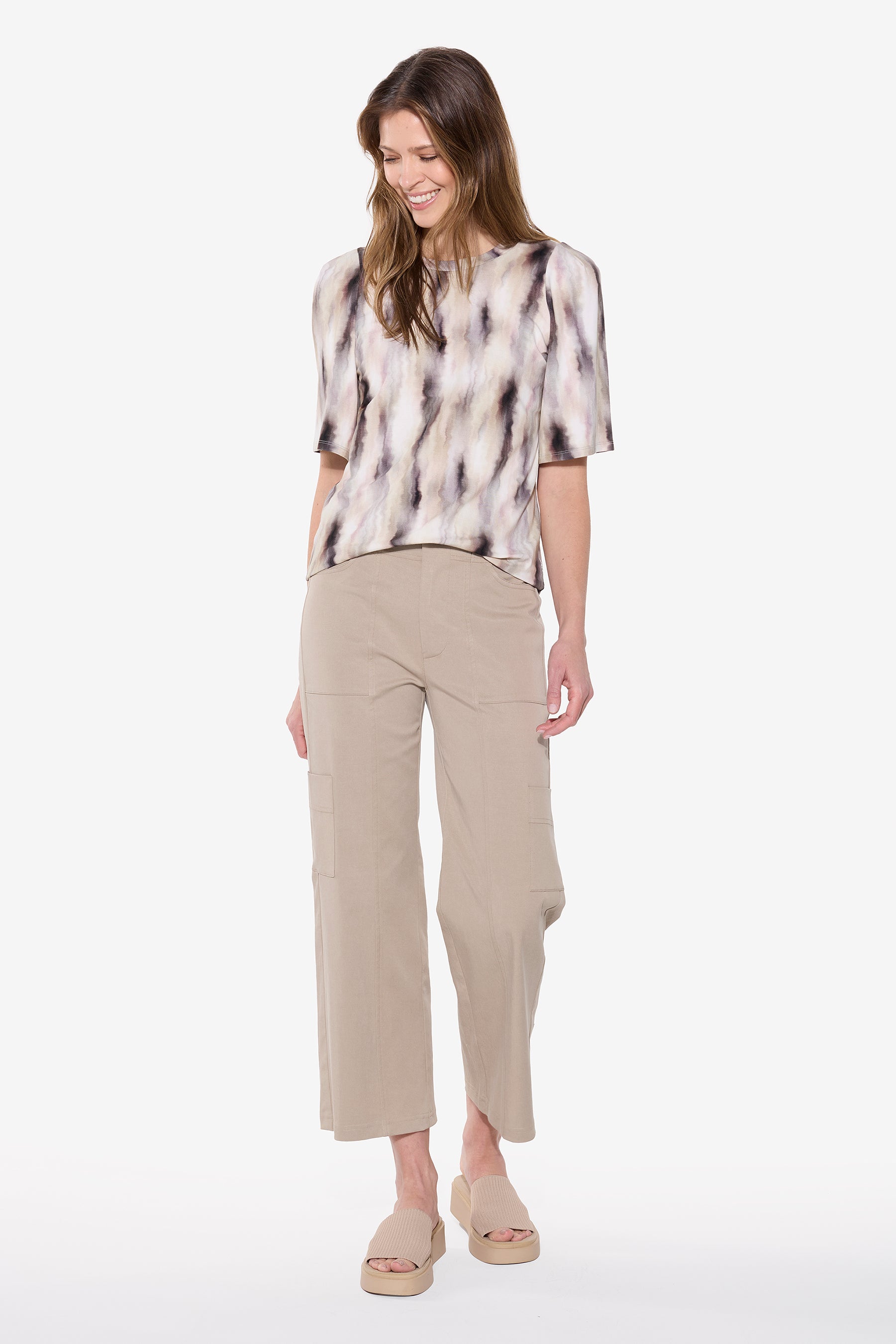 Woman wearing a patterned top and beige pants on a white background