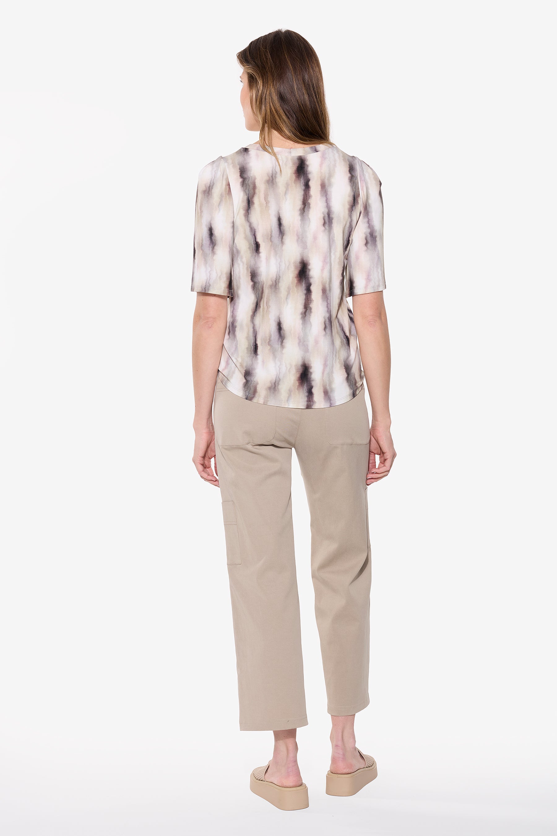Woman wearing a patterned blouse and beige pants on a white background Back View