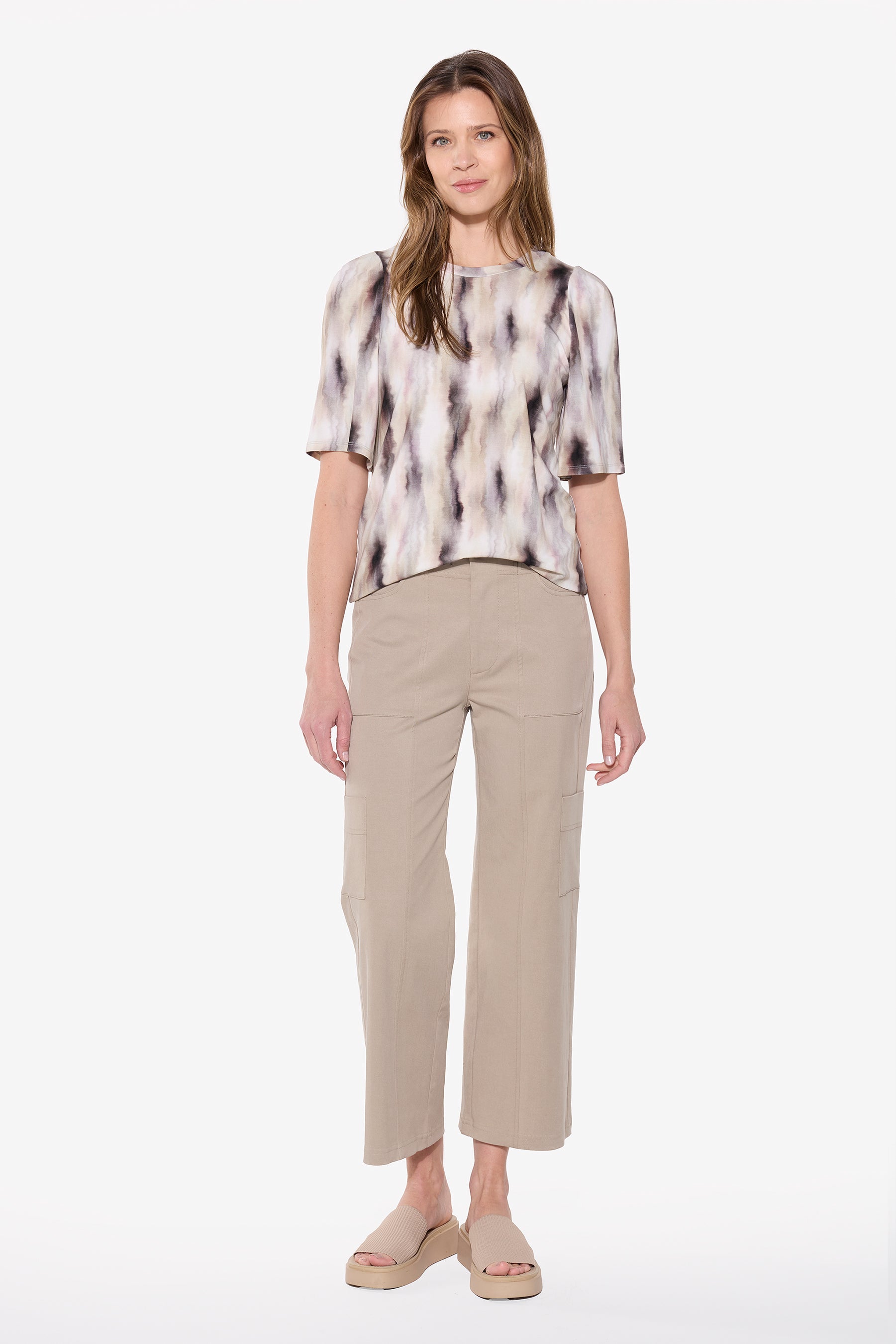 Woman wearing a patterned blouse and beige pants on a white background