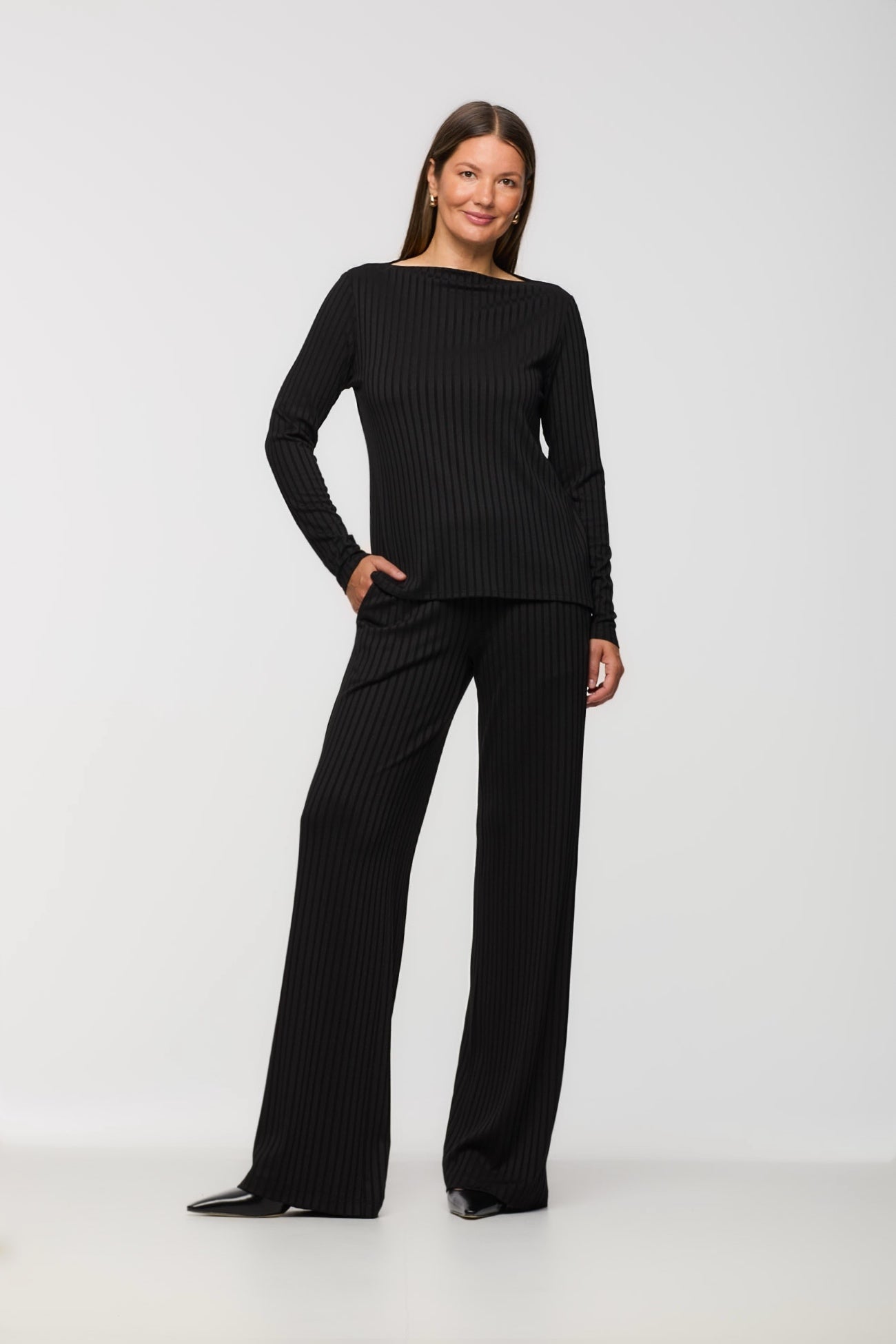 Woman wearing a black ribbed sweater and matching pants on a white background